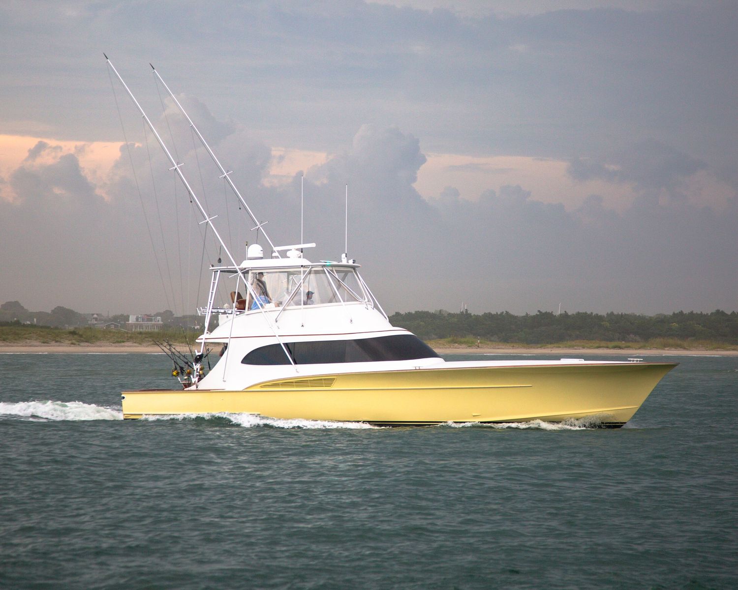 Yellow and white sport fishing boat speeding through coastal waters against cloudy sky.