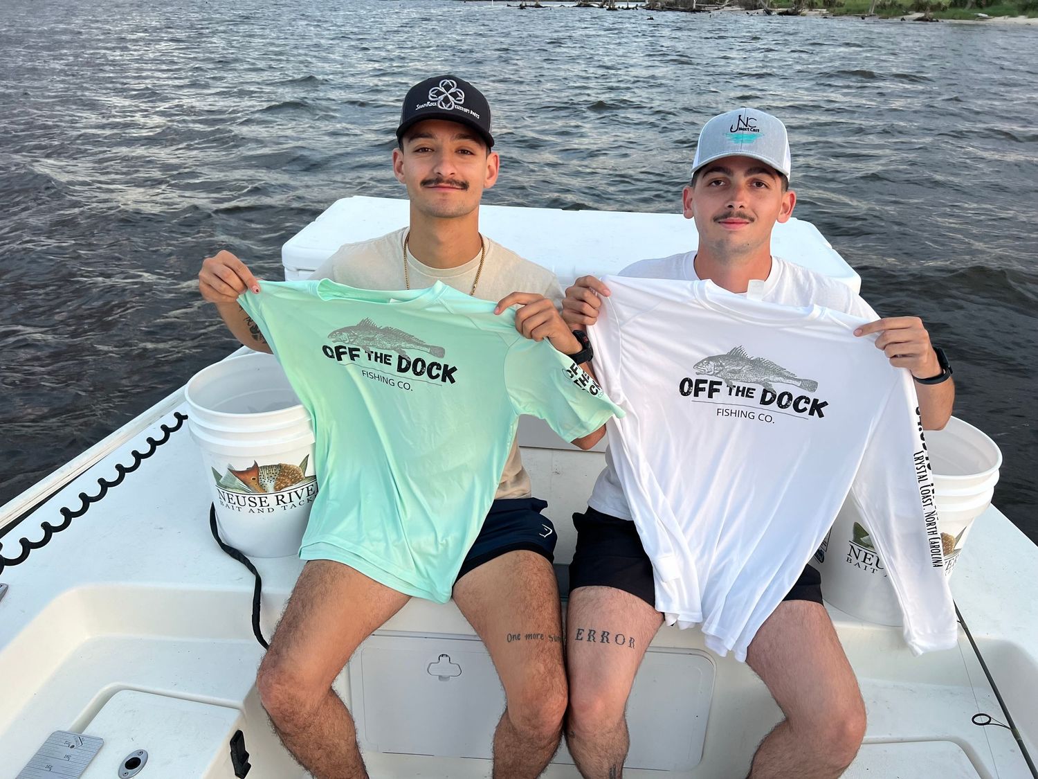 Two anglers showing off matching t-shirts while sitting in a fishing boat.