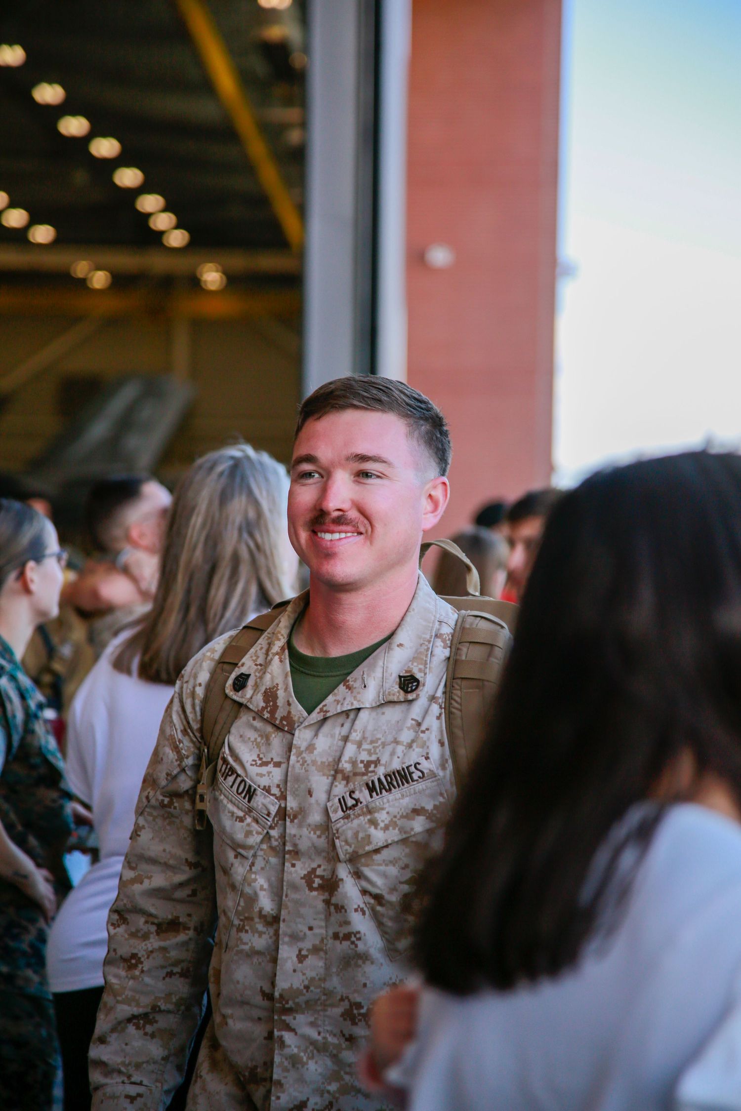 U.S. Marines in desert camouflage uniforms gather indoors during a military event.