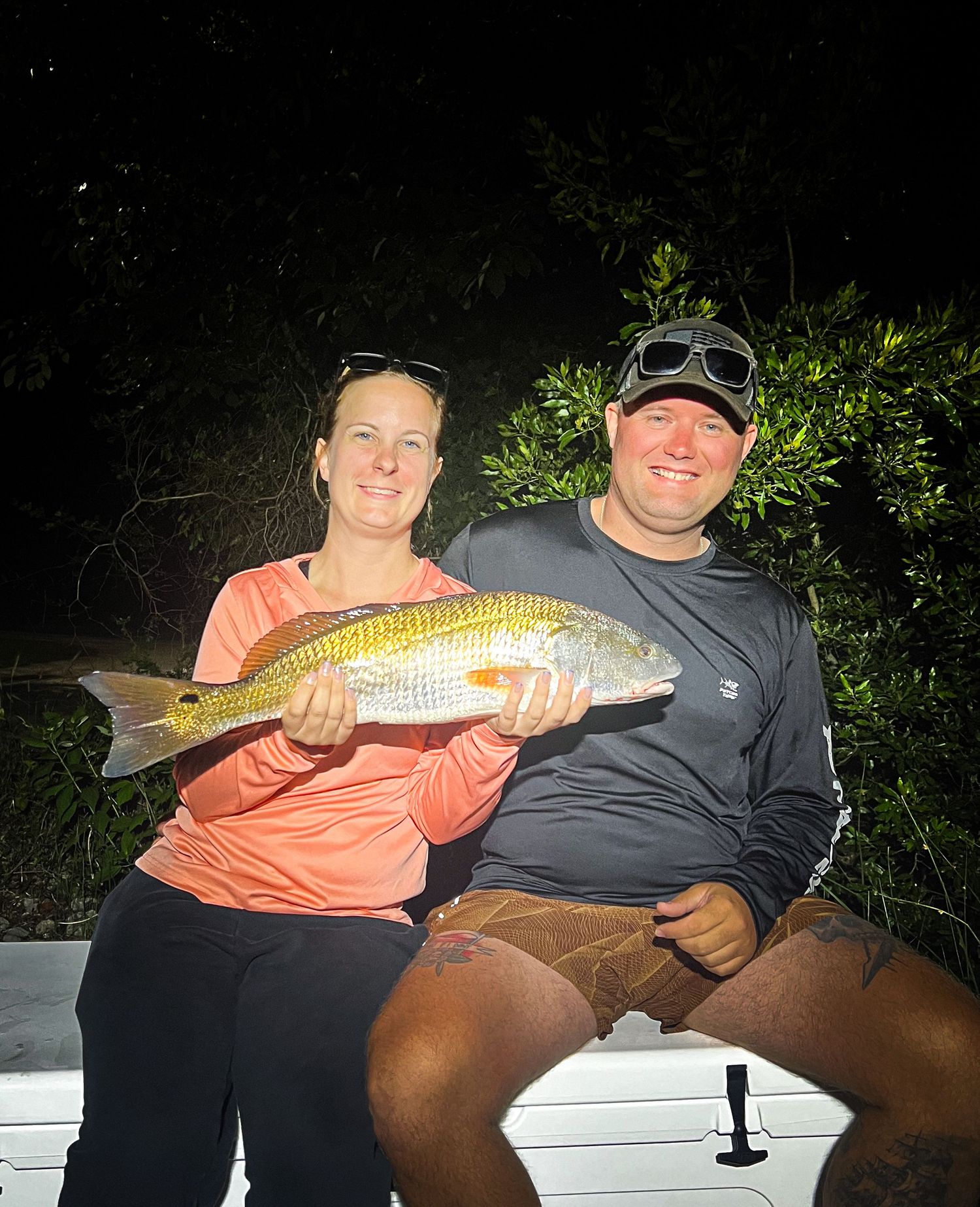 Couple smiling at night holding a large redfish caught during a nighttime fishing trip outdoors.