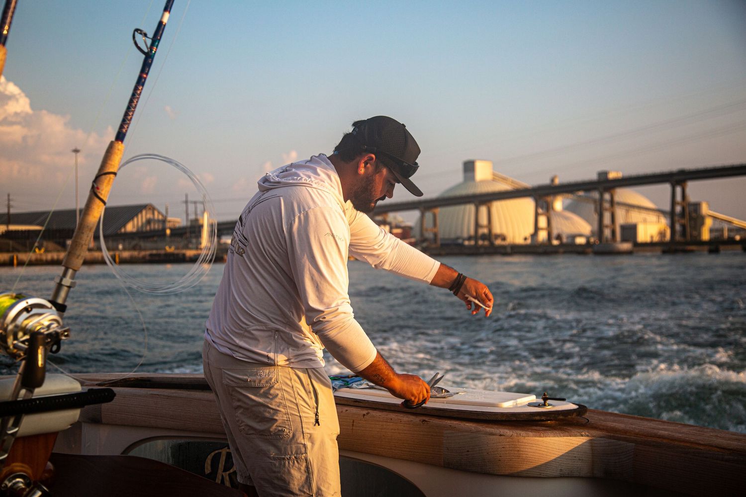 Fisherman on a boat preparing fishing gear near a bridge at sunset over calm waters.