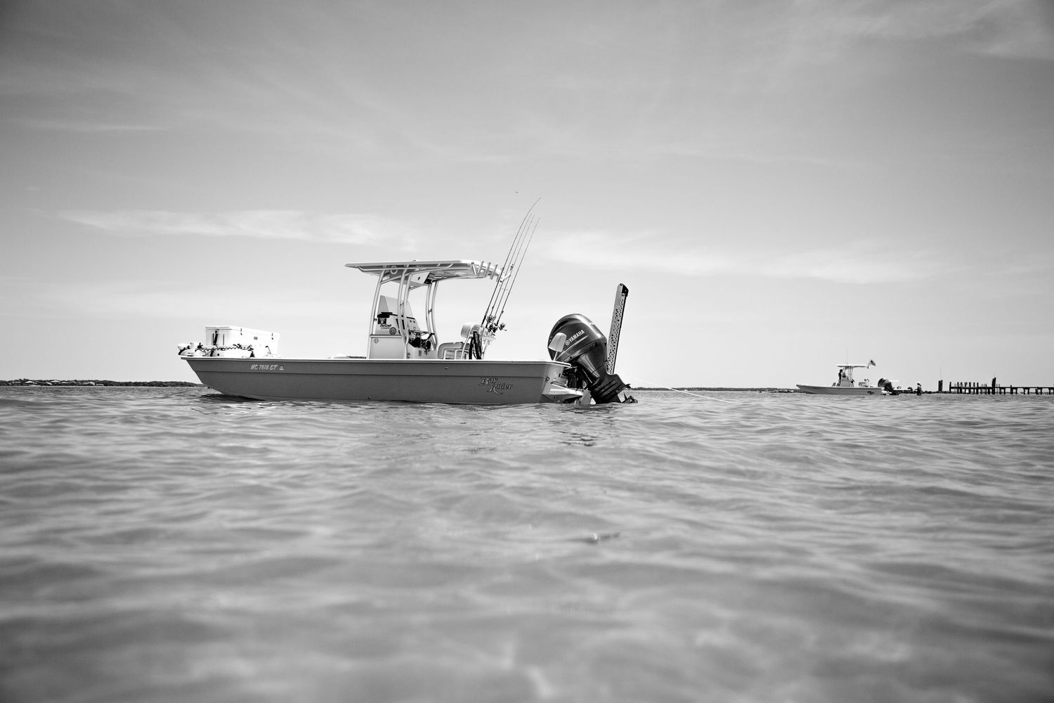 Boats cruising across calm waters against a bright horizon in black and white.