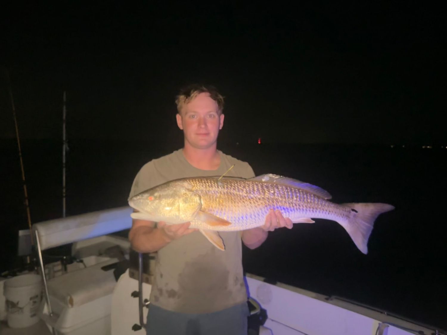 Nighttime angler displays large redfish catch illuminated by boat lights.