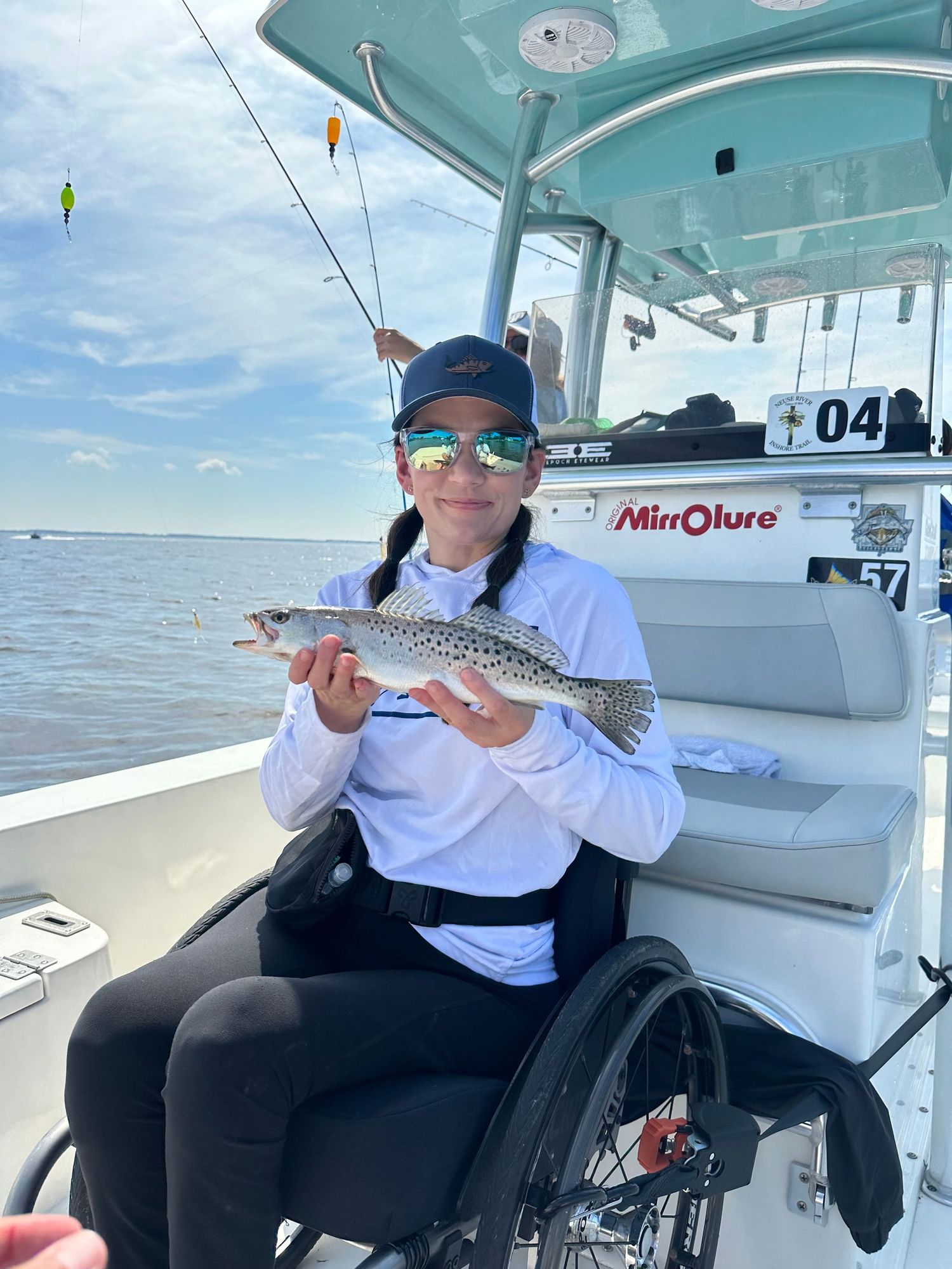 Wheelchair user displaying a caught fish while aboard a fishing boat.