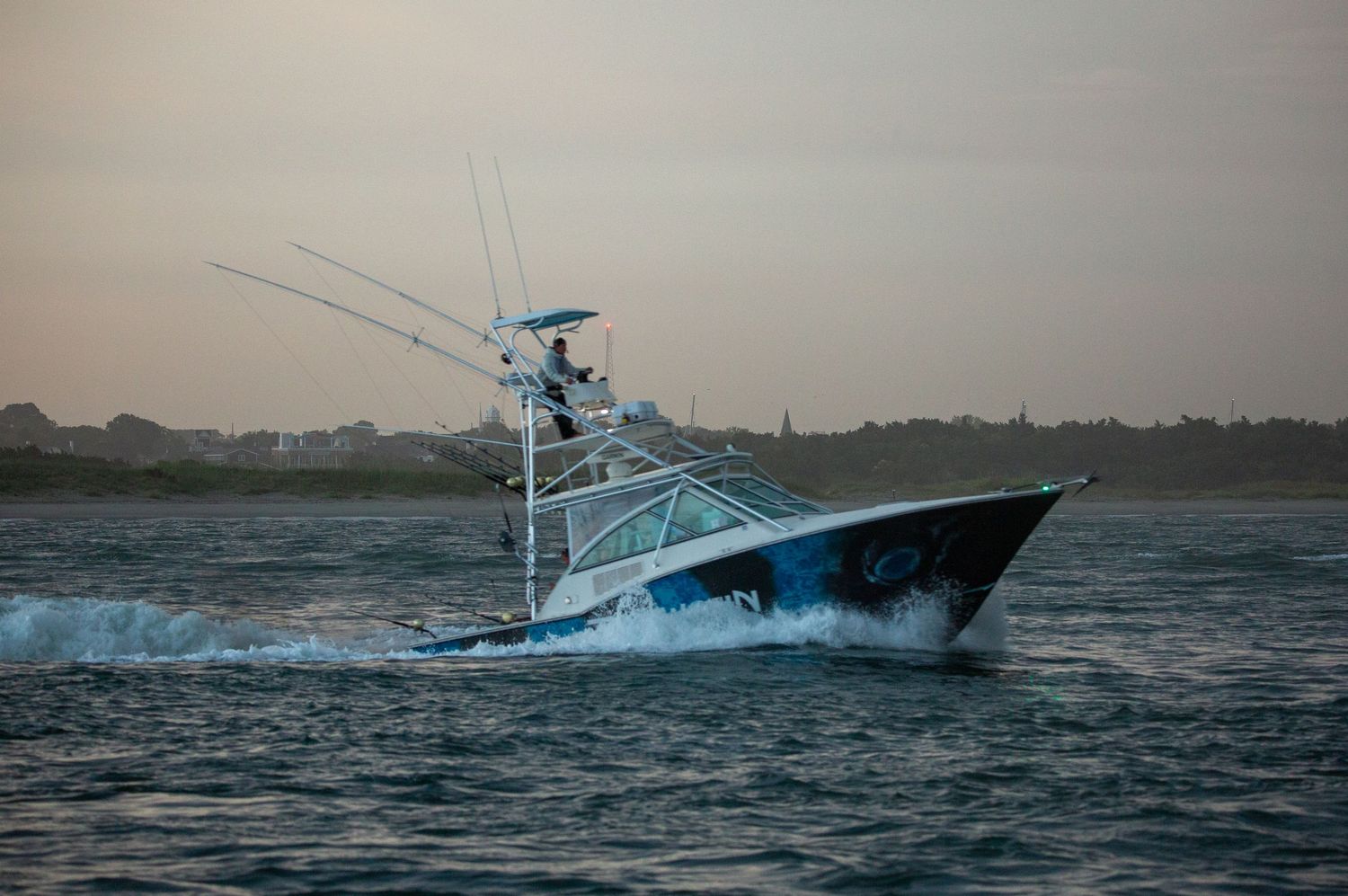 Deep sea fishing vessel powers through choppy waters with blue hull visible in coastal setting.