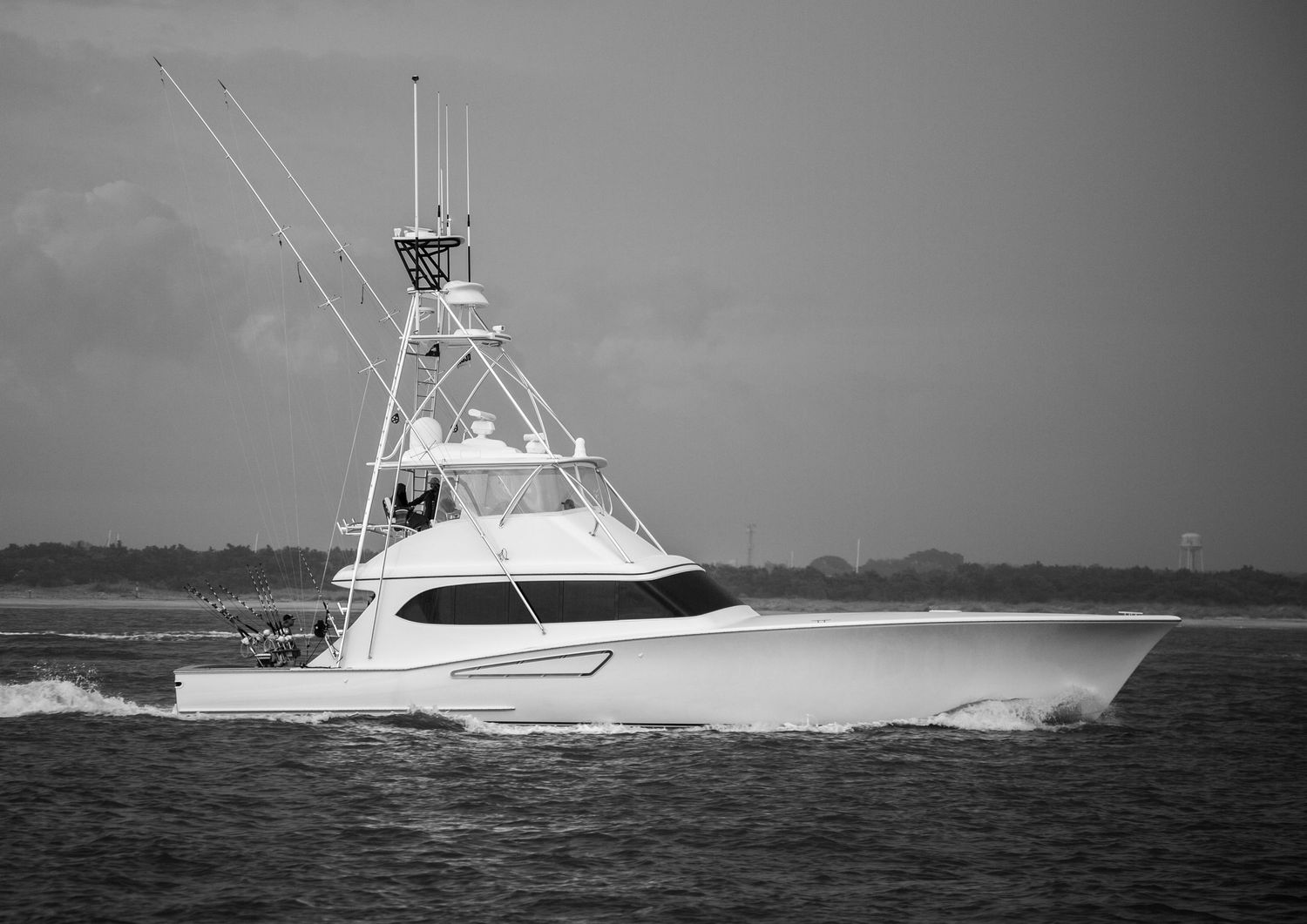 Sports fishing yacht cruising through calm ocean waters on a cloudy day.