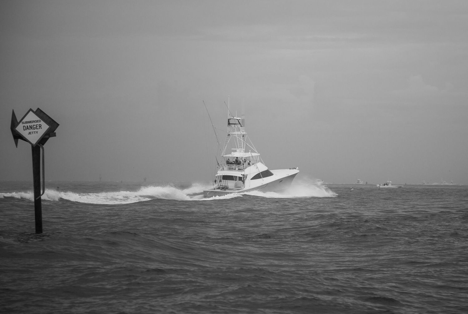 Fishing vessel cuts through stormy waters in black and white photography.
