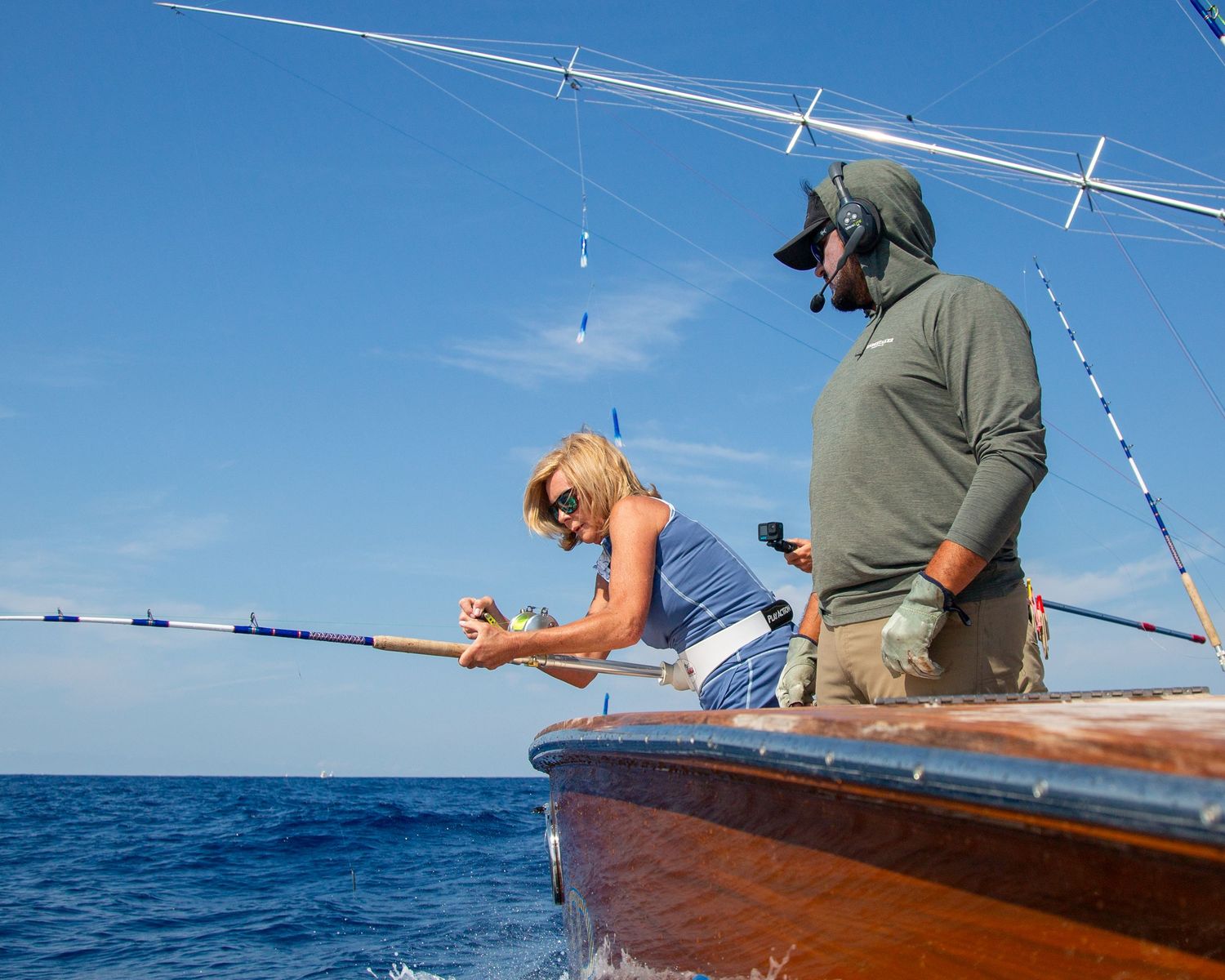 Two anglers fishing from a wooden boat on calm blue ocean waters on a sunny day.