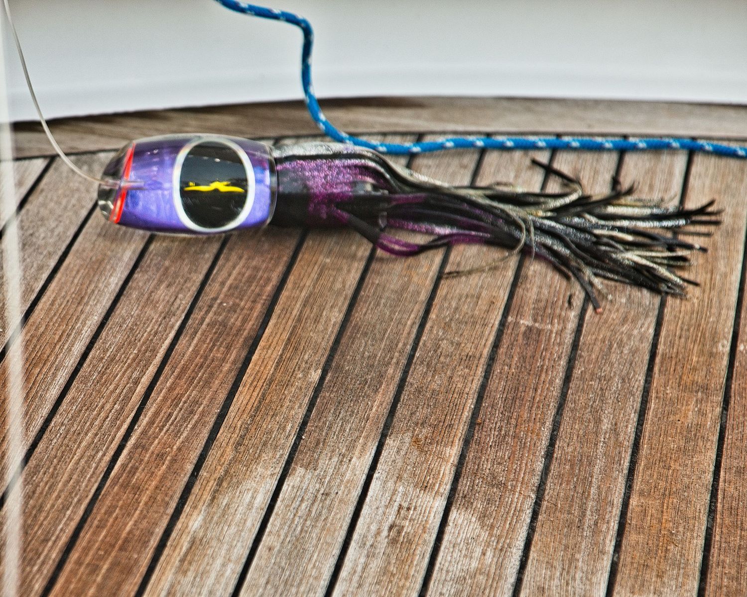 Colorful fishing lure with purple skirt and blue rope on wooden boat deck.