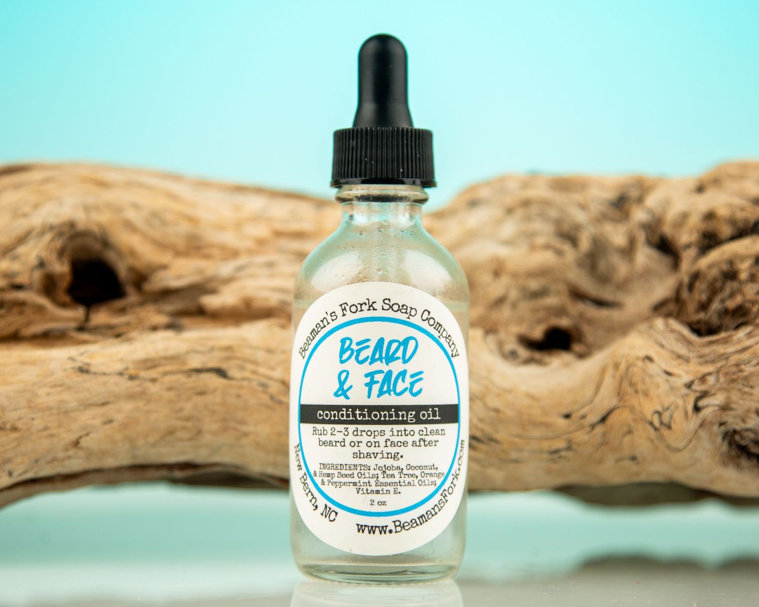 Beard & Face conditioning oil by Swamp Frog Soap Co. in a 2oz dropper bottle displayed on driftwood.