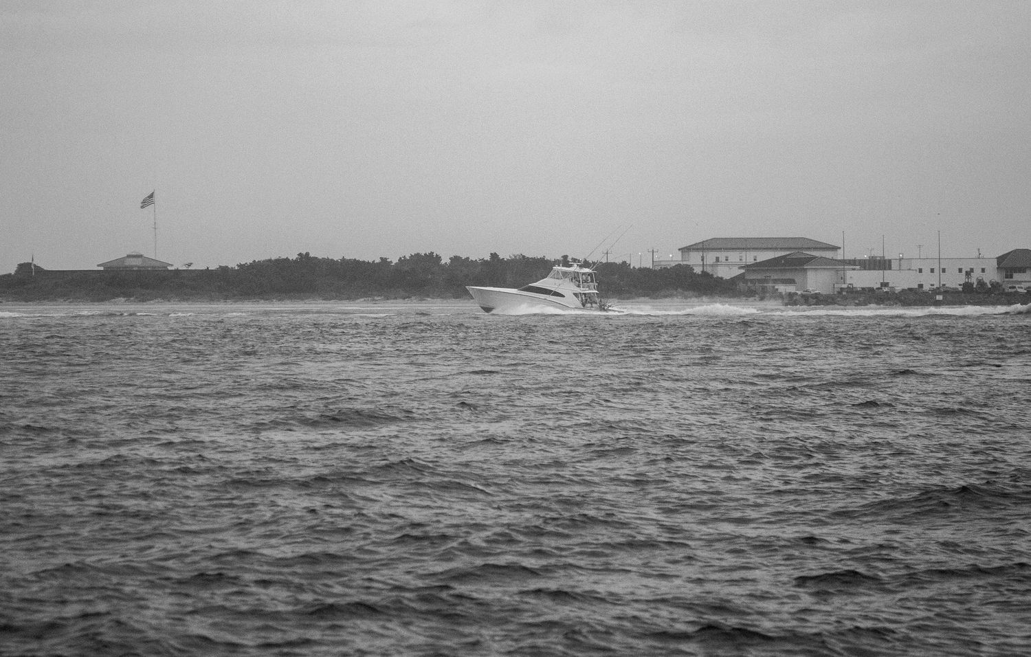 Sport fishing vessel navigating through rough waters with coastal buildings in the distance.