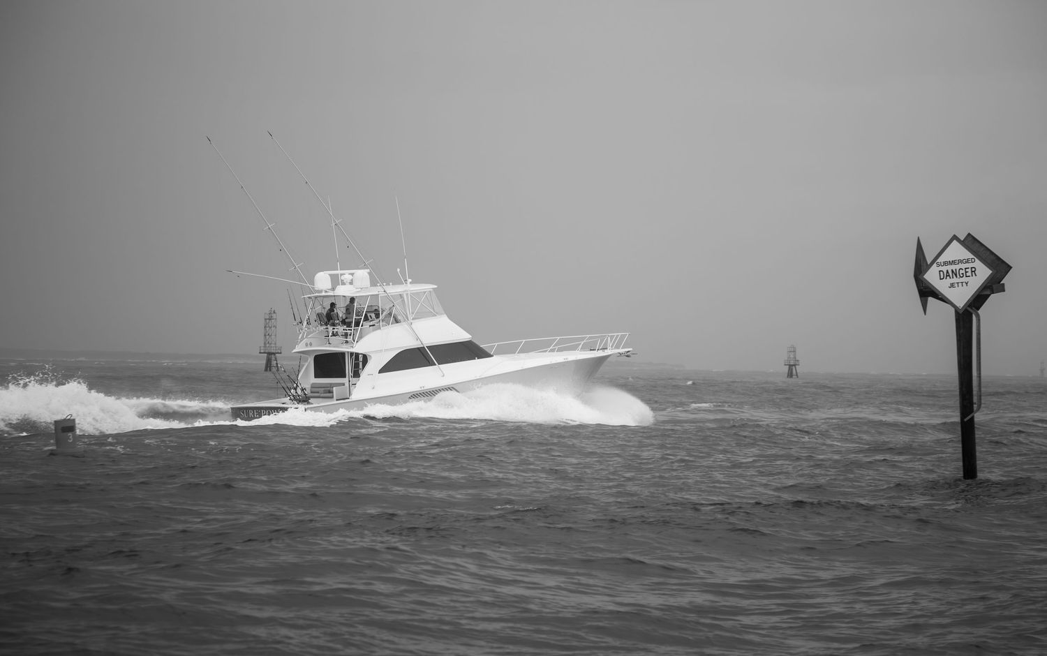 Sport fishing boat navigates through stormy seas past channel marker in black and white.