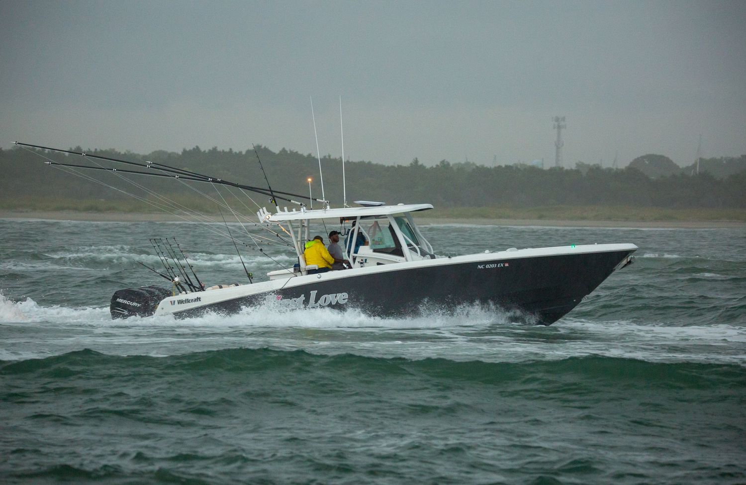 Black center console fishing boat powers through choppy coastal waters.