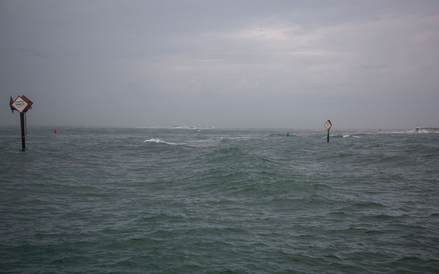Channel markers stand in rough seas with boats visible on the stormy horizon.