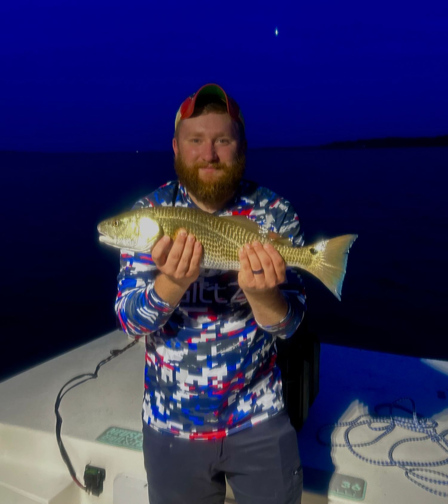 Proud catch of a golden redfish at night with deep blue sky background.