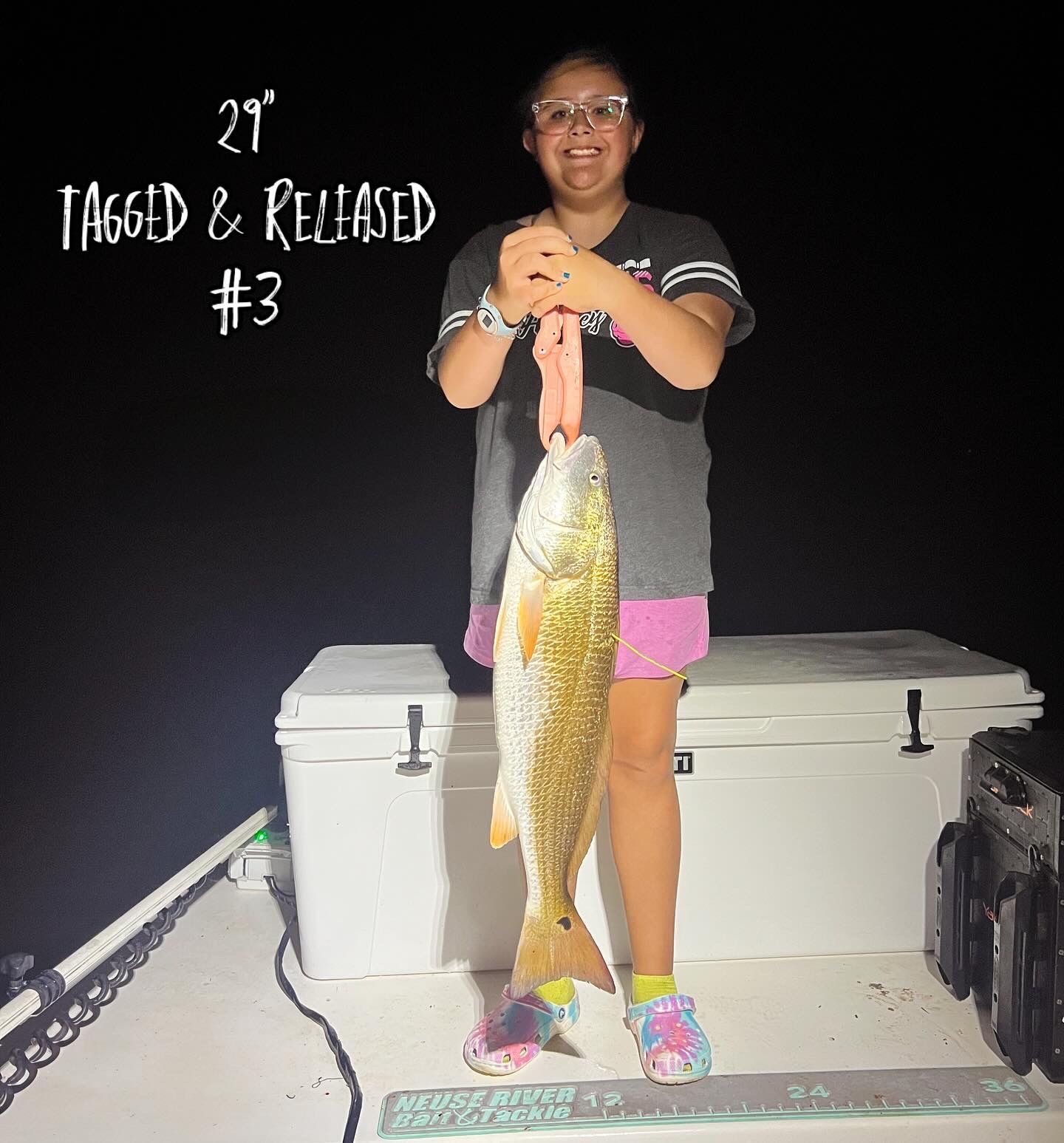 Nighttime fishing success with a large redfish caught on the boat deck with coolers in background.