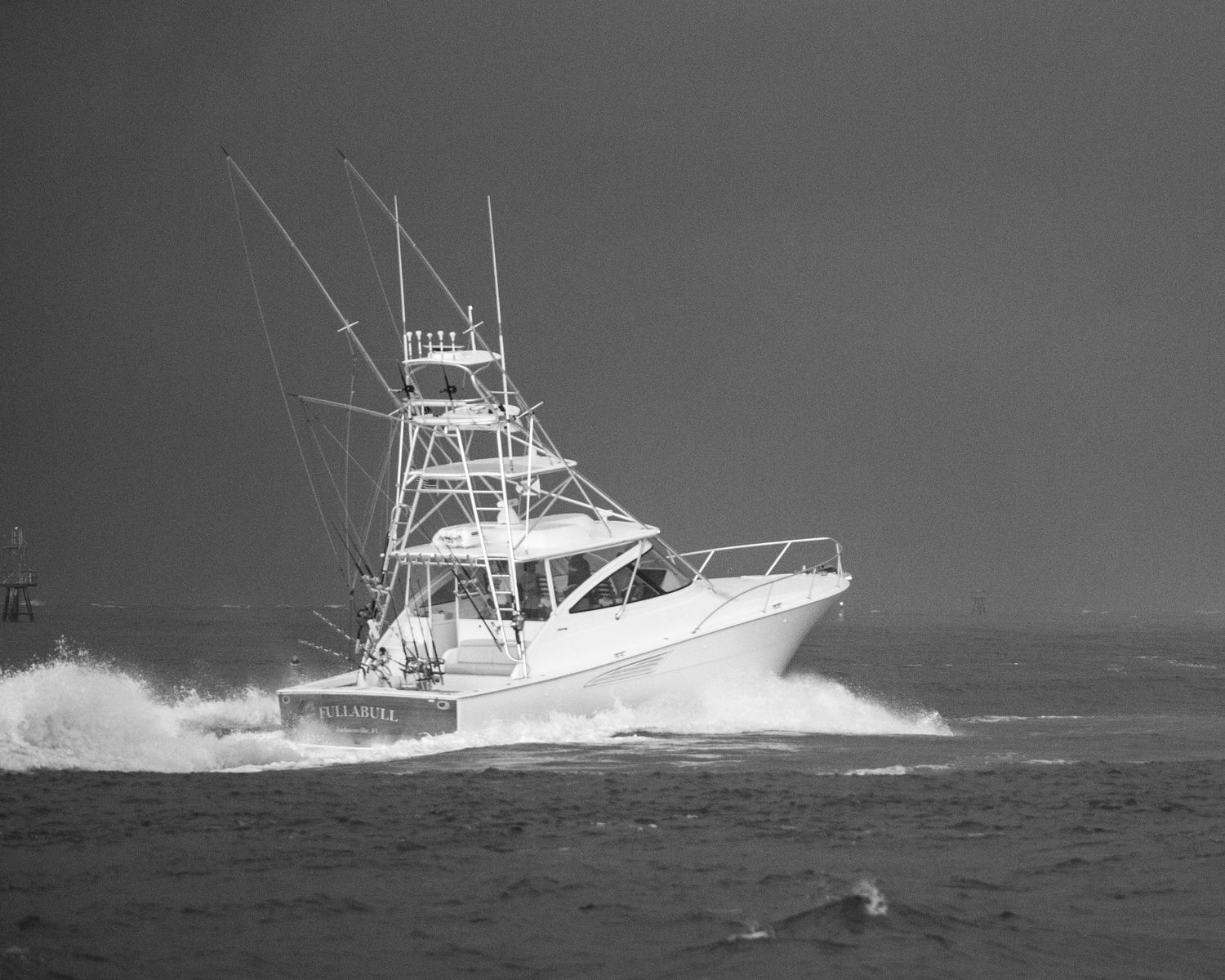 Large sport fishing boat powers through rough ocean waves in monochrome photography.