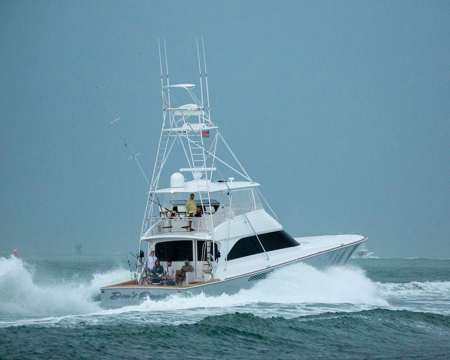 Large sport fishing yacht crashes through ocean waves during rough weather conditions.
