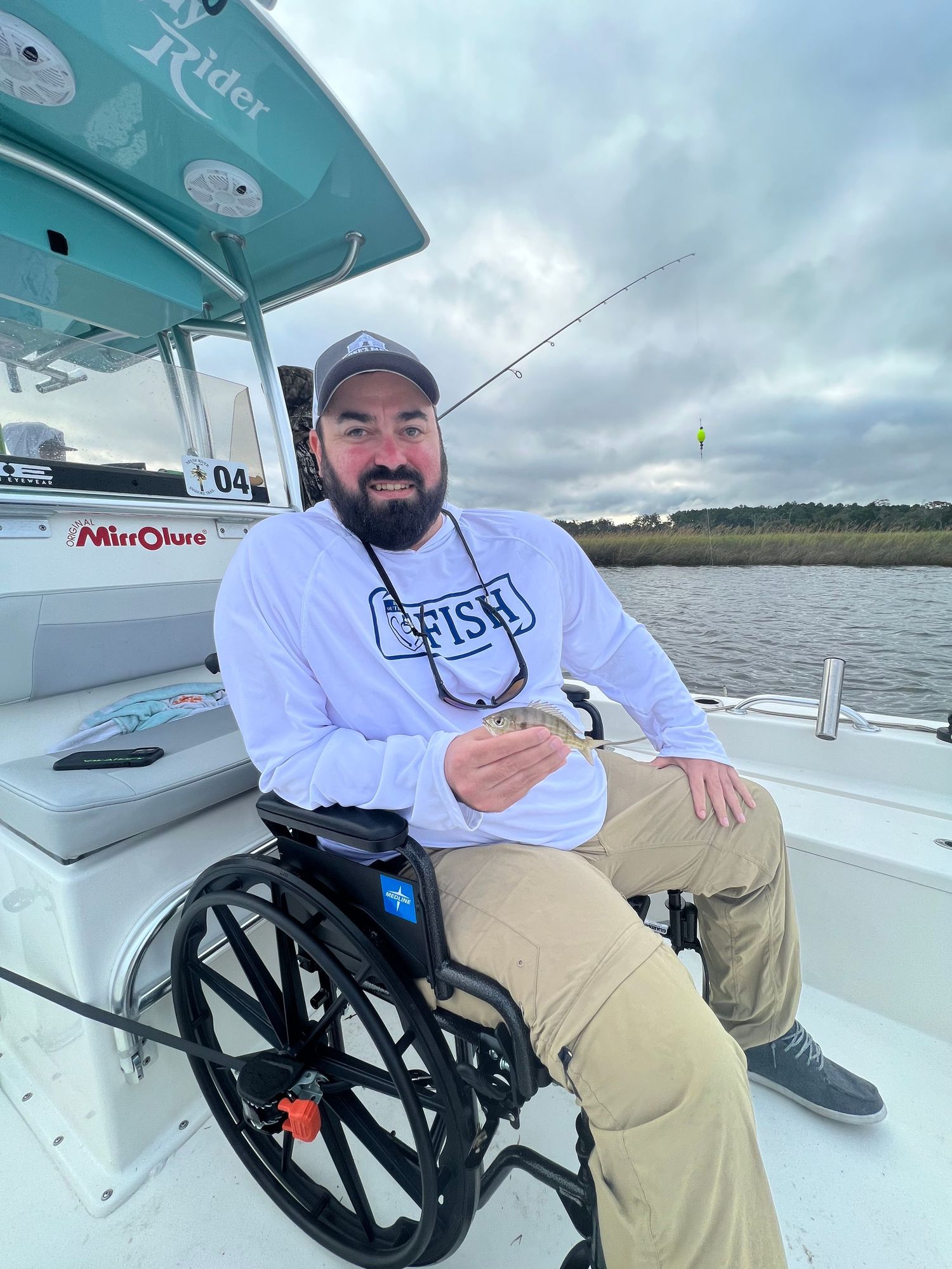 Fishing expedition participants showing their catches while seated in wheelchairs.