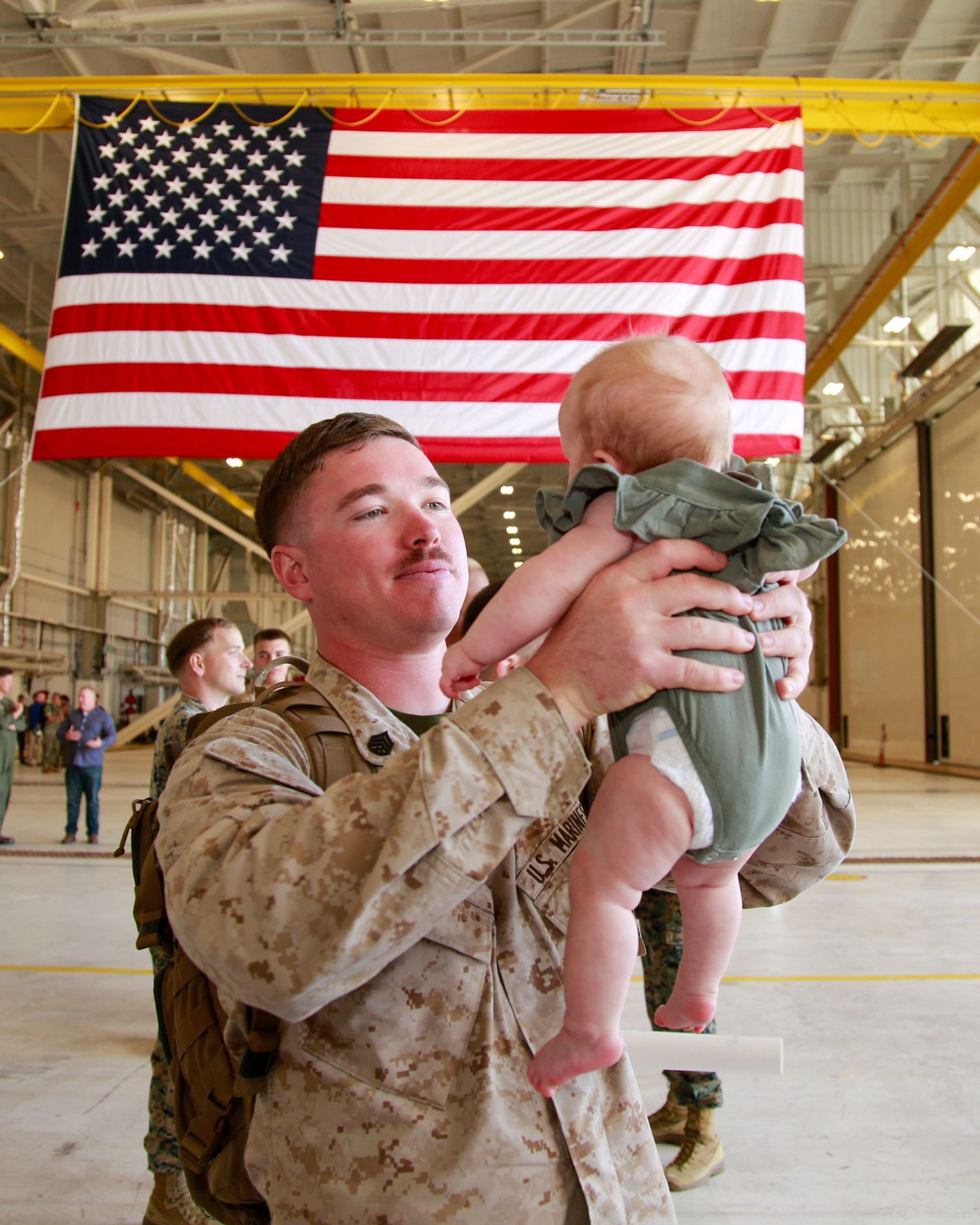 Marines in desert camo uniforms stand at attention under American flags during a formal ceremony.