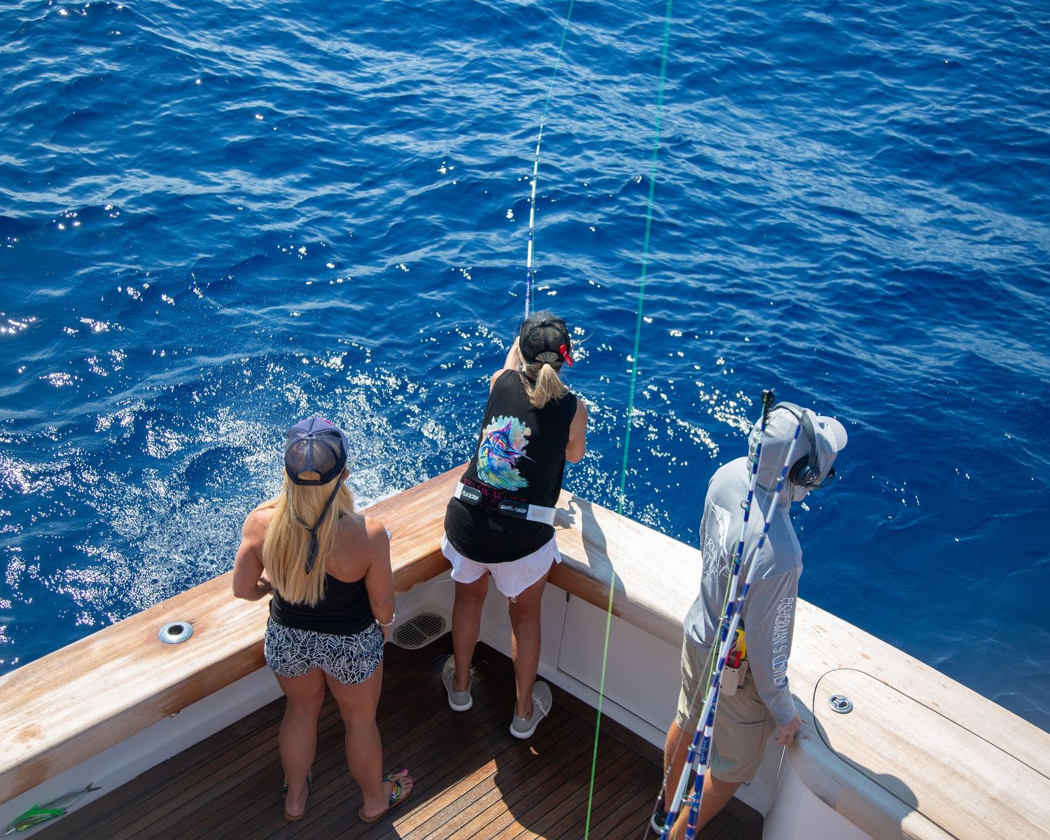 Two women fishing from the stern of a boat on deep blue ocean waters on a sunny day.