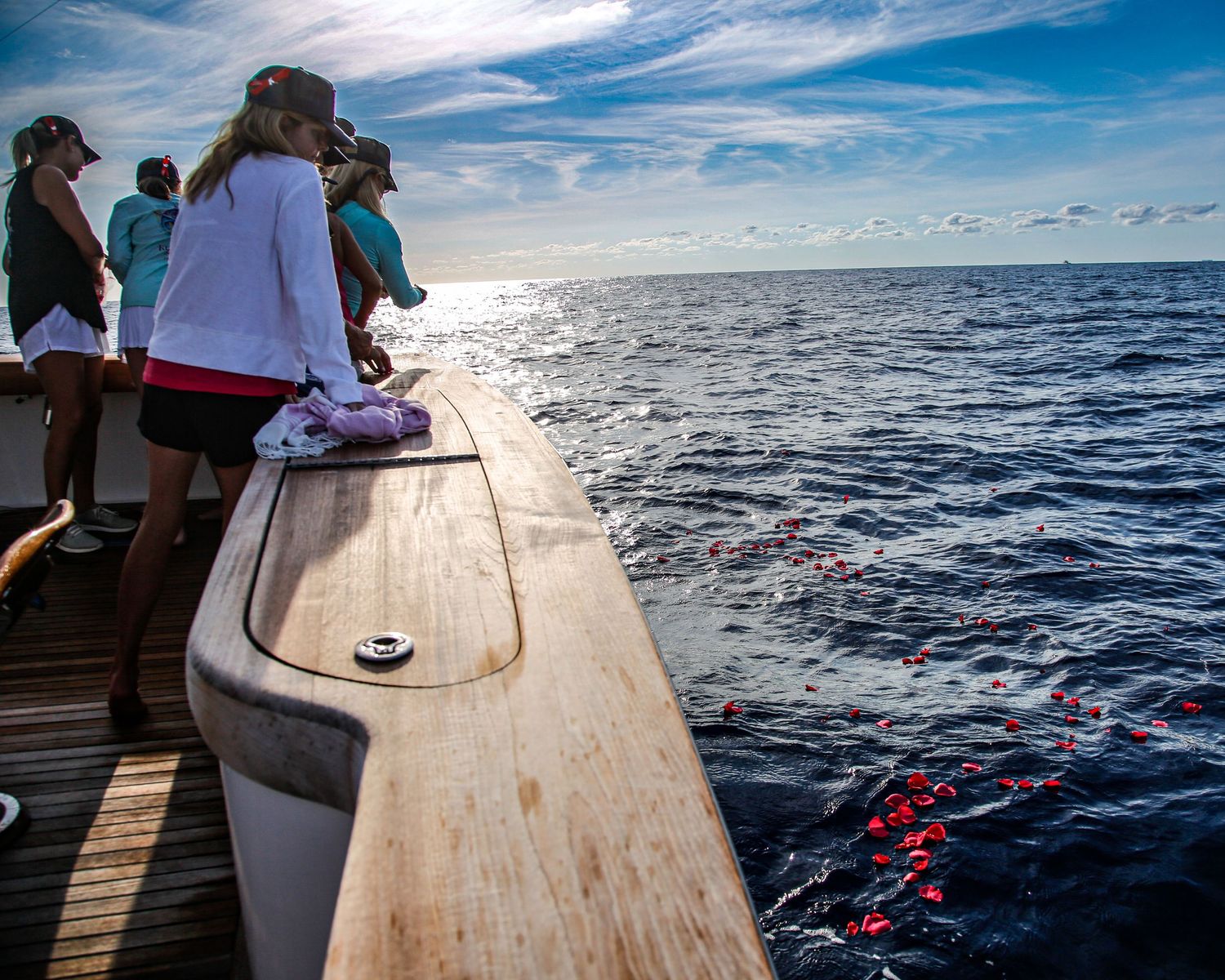 People standing on a boat deck watching red buoys floating in the ocean on a sunny day.