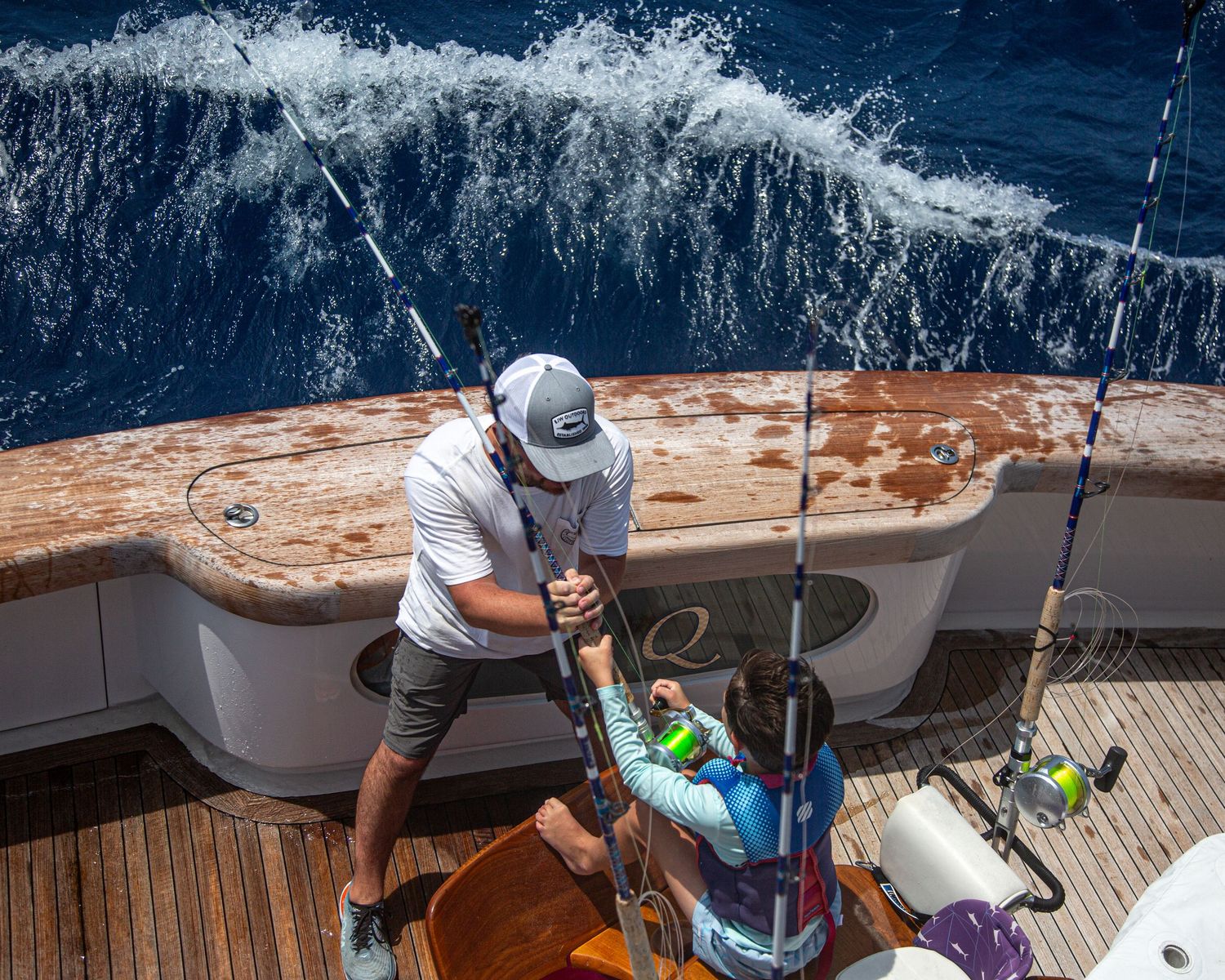 Man in white shirt reeling in a catch on a deep sea fishing yacht.
