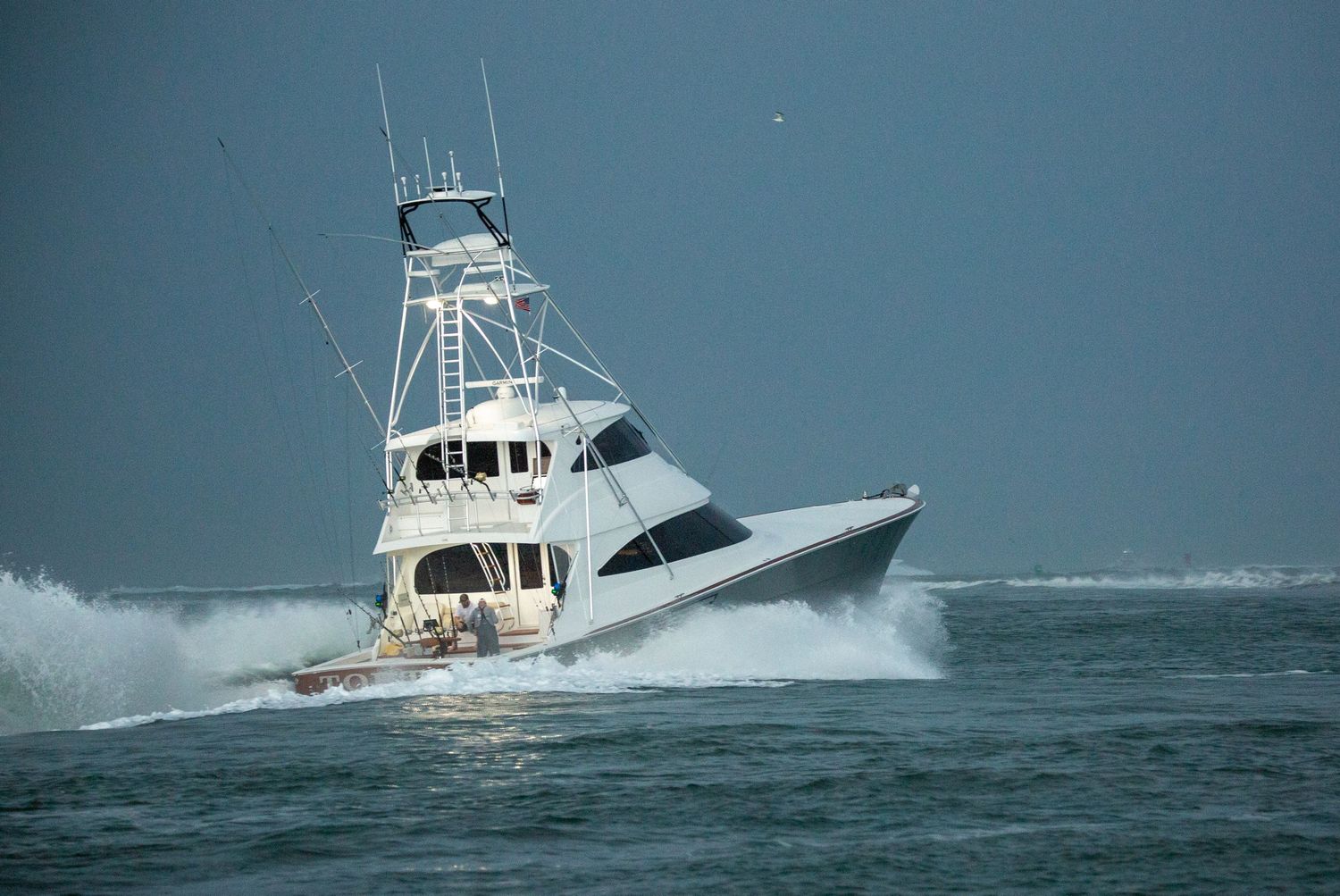 Large white sportfishing yacht crashing through ocean waves at high speed.