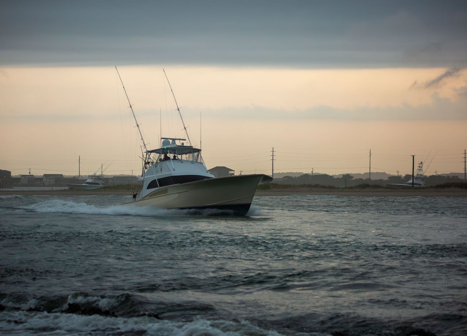 Sport fishing boat cruises through choppy waters at sunset with fishing poles mounted on top.