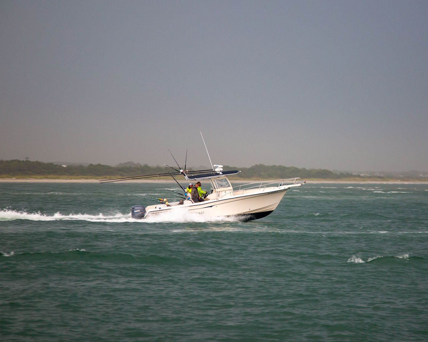 White center console fishing boat cruises through choppy coastal waters on a cloudy day.