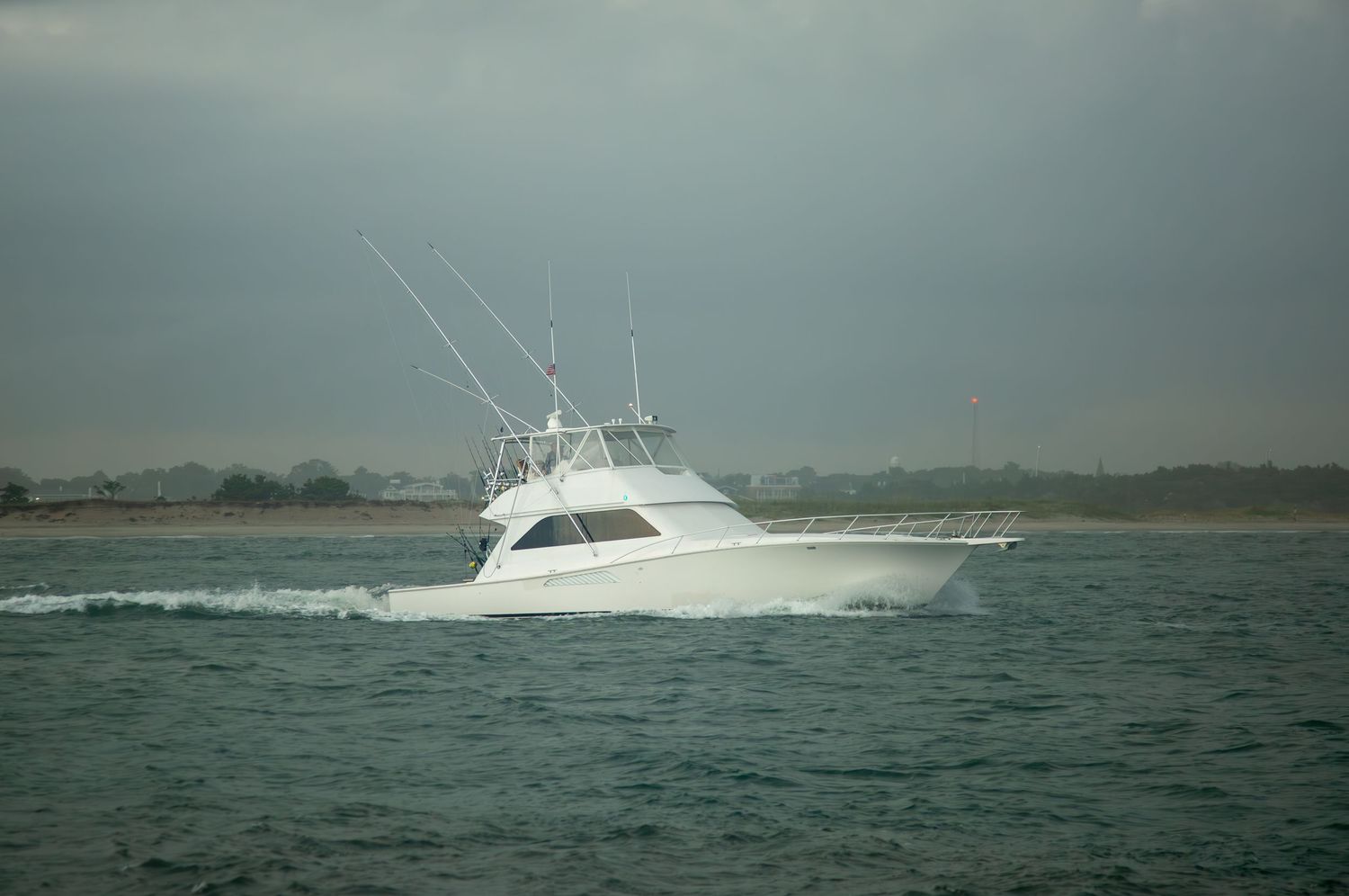 White sportfishing yacht cruising through choppy waters on an overcast day.