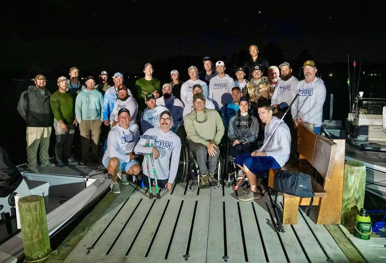Large group of anglers gathered on a wooden dock at night after a fishing expedition with Disabled Outdoorsmen event.
