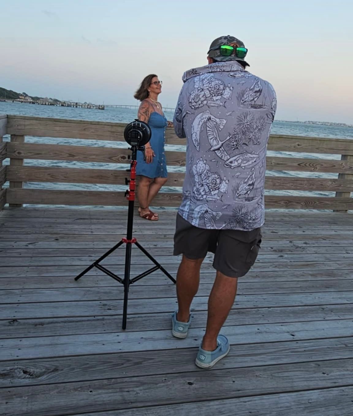 People on a wooden pier setting up photography equipment at dusk.