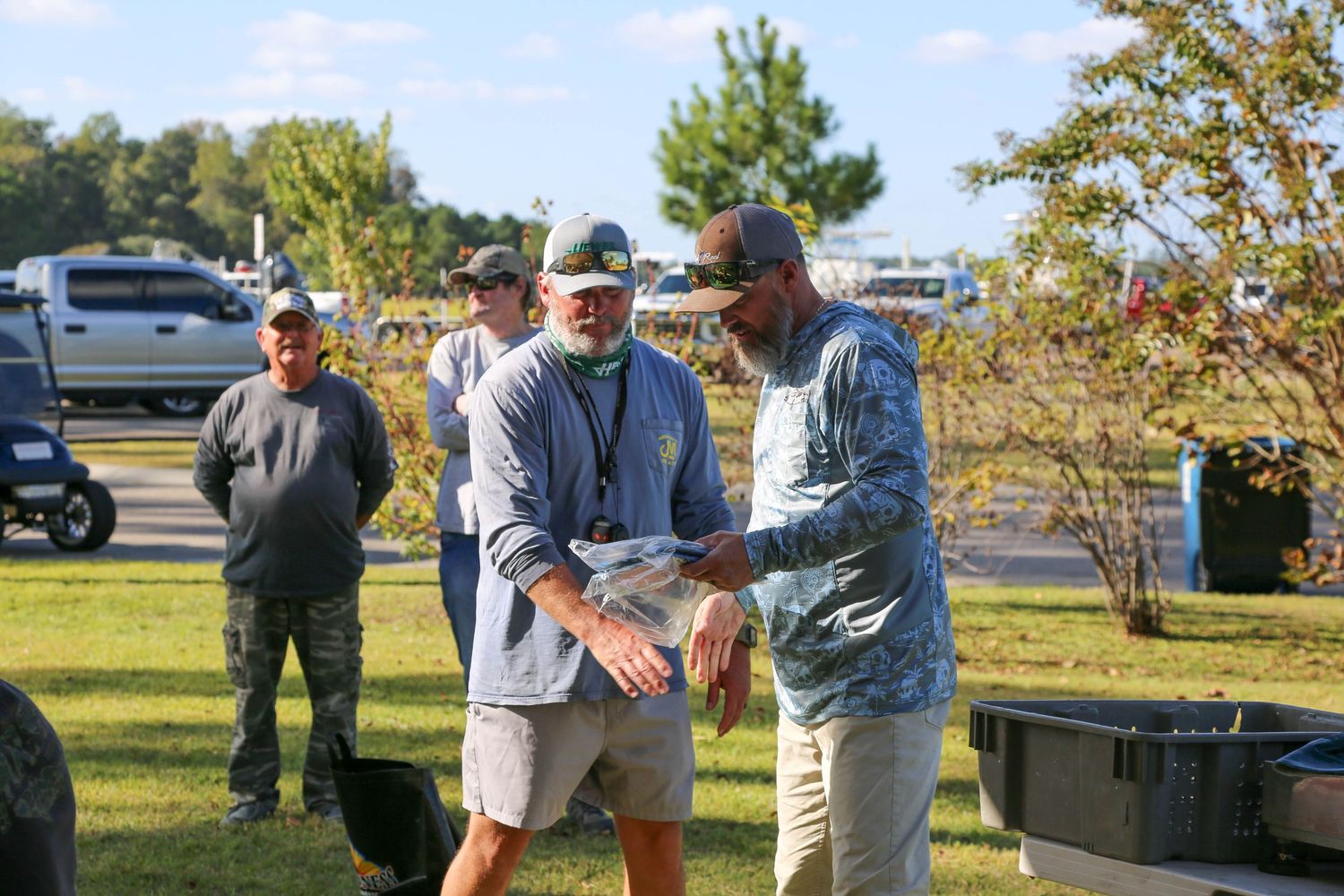Three people having casual conversation outdoors at fishing event.
