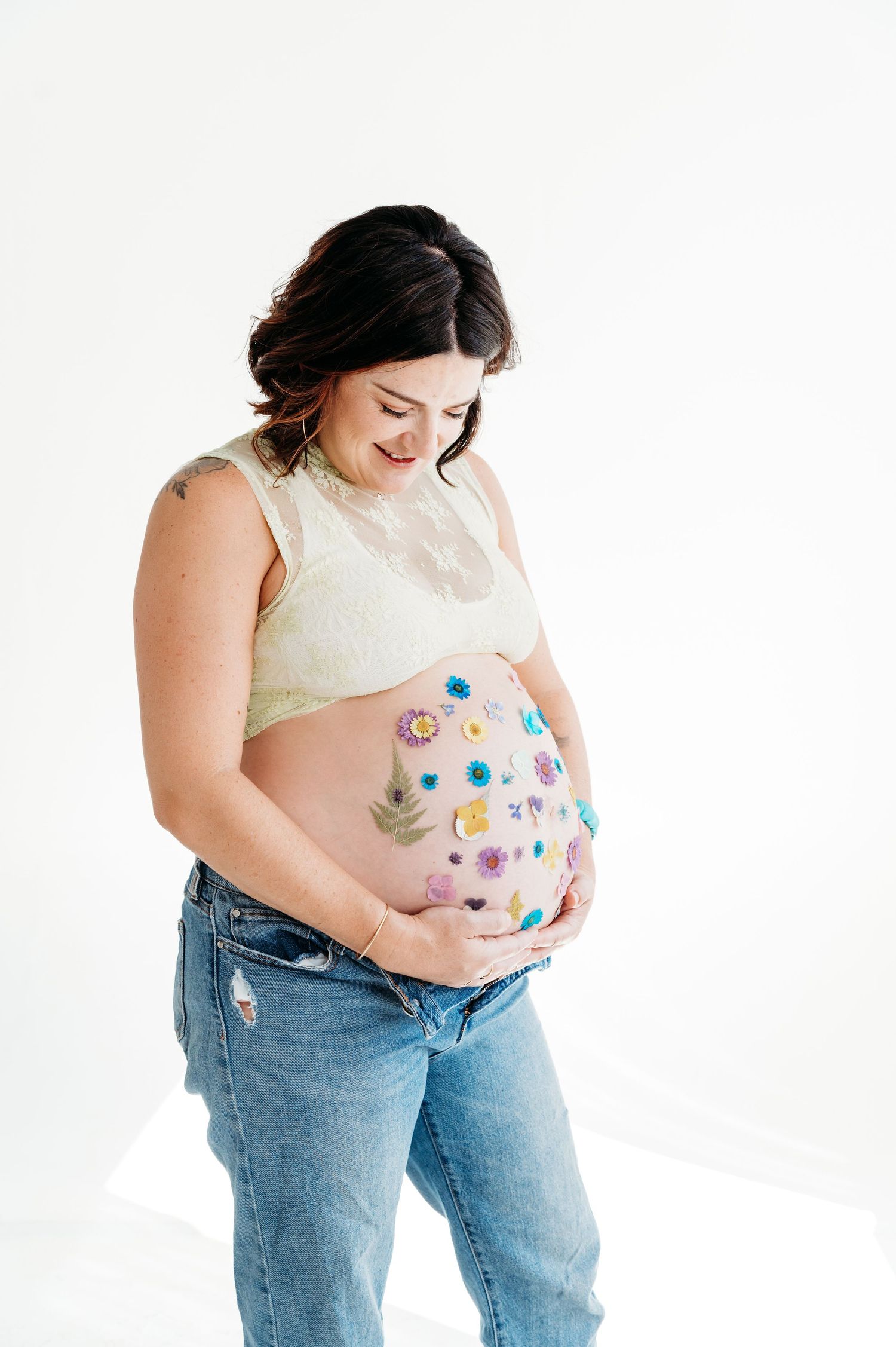 Artistic maternity photo showing pregnant woman in jeans and white top with colorful floral painted belly.
