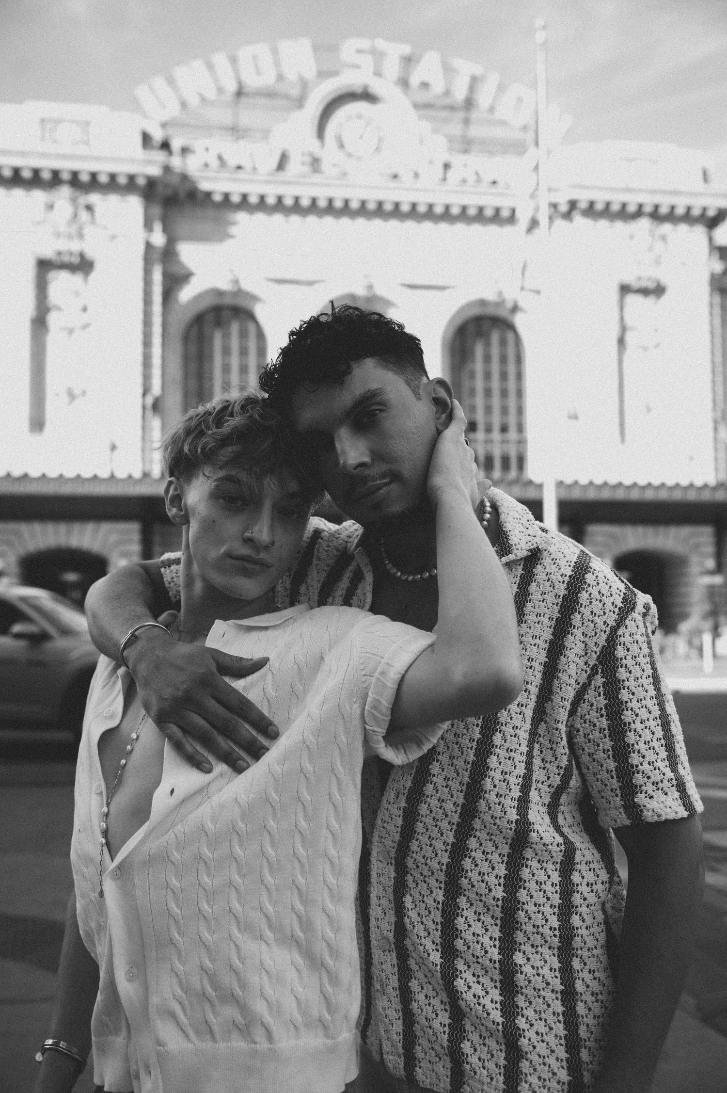 Two young men pose affectionately in front of Union Station in a black and white photo.
