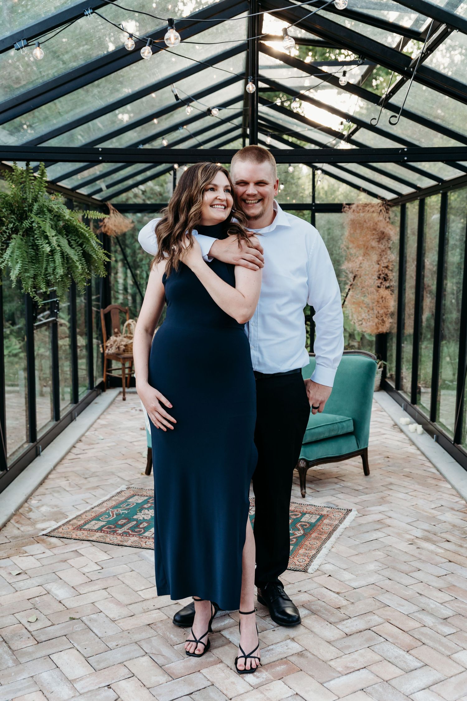 A couple shares a romantic moment in an elegant glass greenhouse with brick floor and turquoise accent chair.