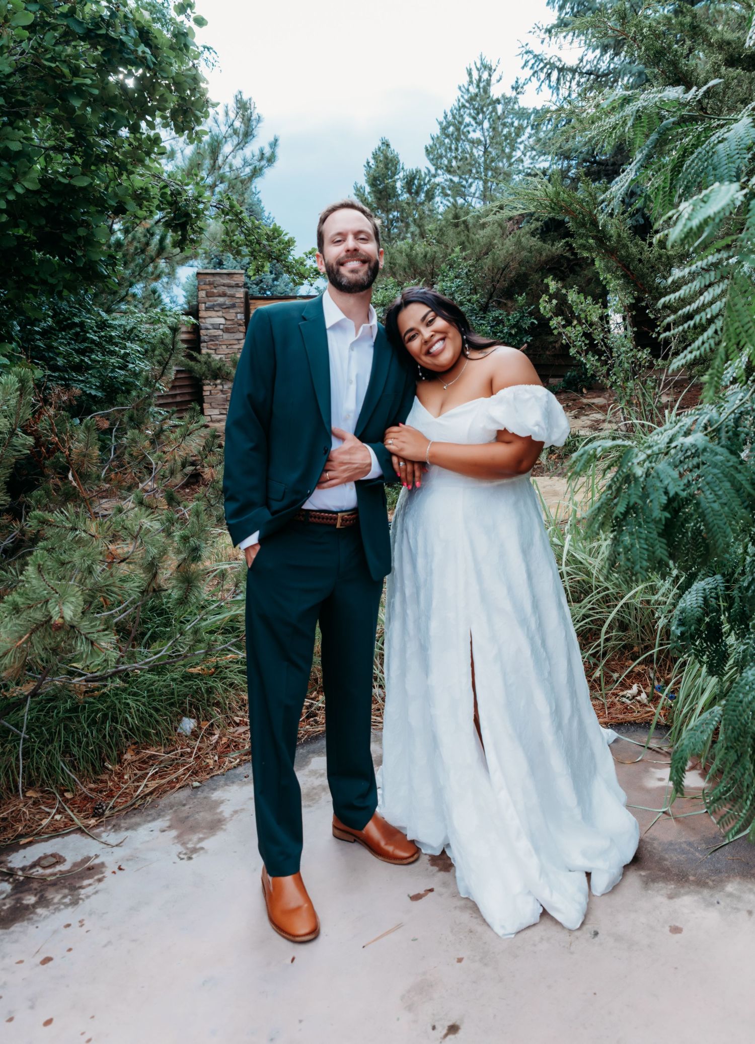 A couple shares a romantic moment on a garden path surrounded by lush greenery during their wedding photoshoot.