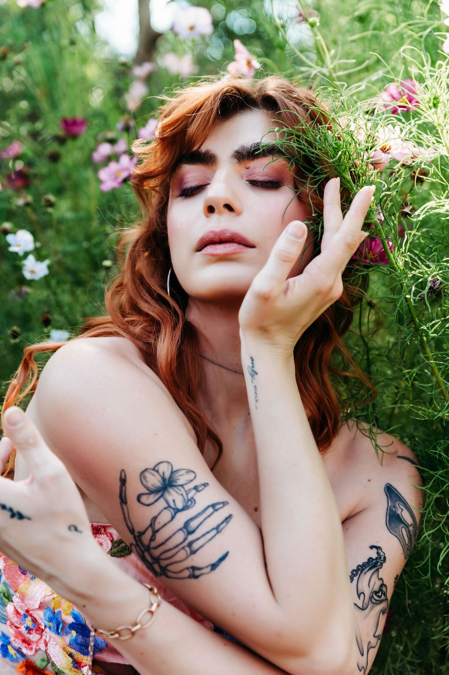 Portrait in garden with tattoos and flowers, eyes closed in dreamy pose.