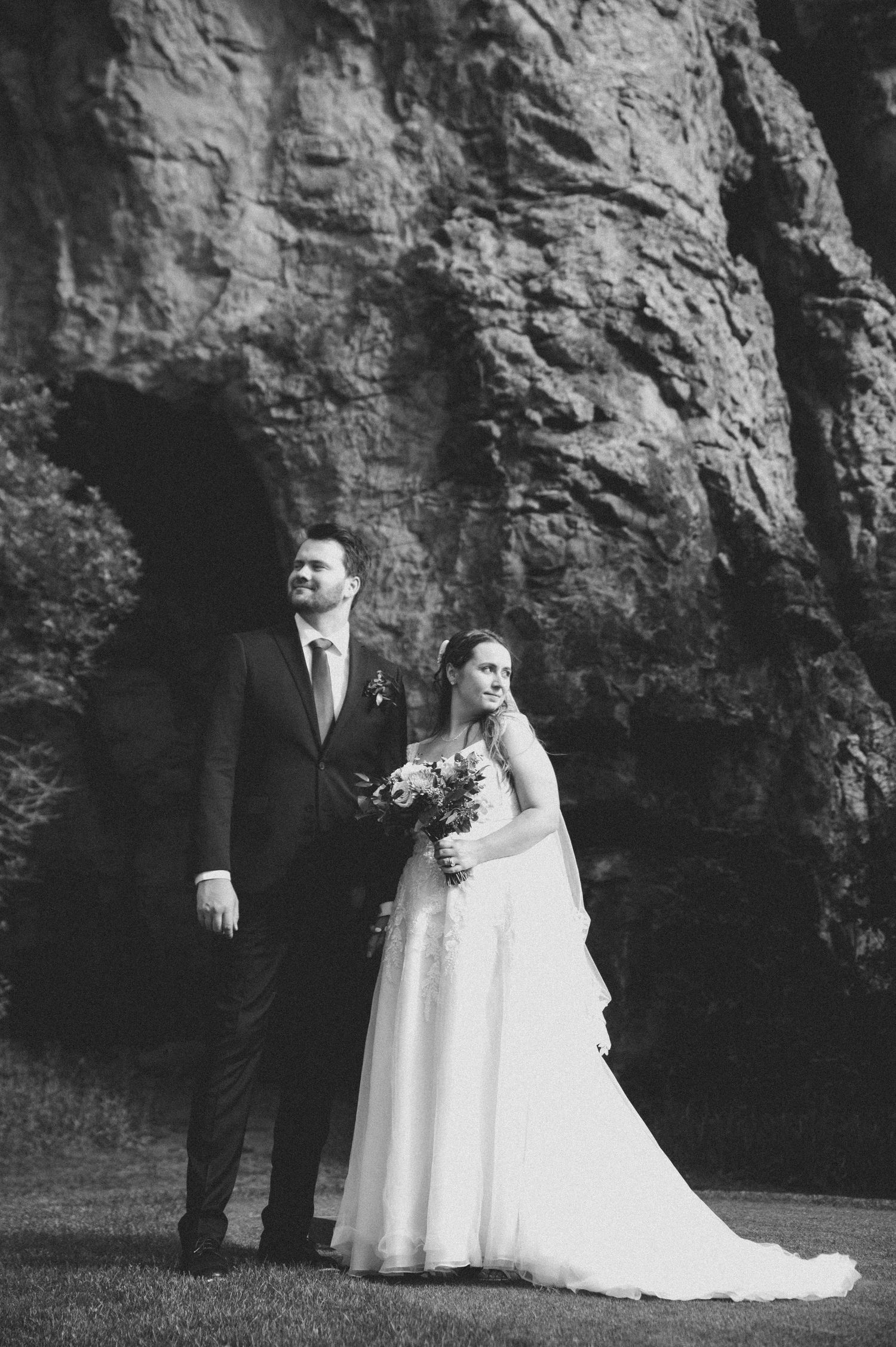 A romantic black and white wedding photo series showing a couple posing against a dramatic rocky cliff backdrop.