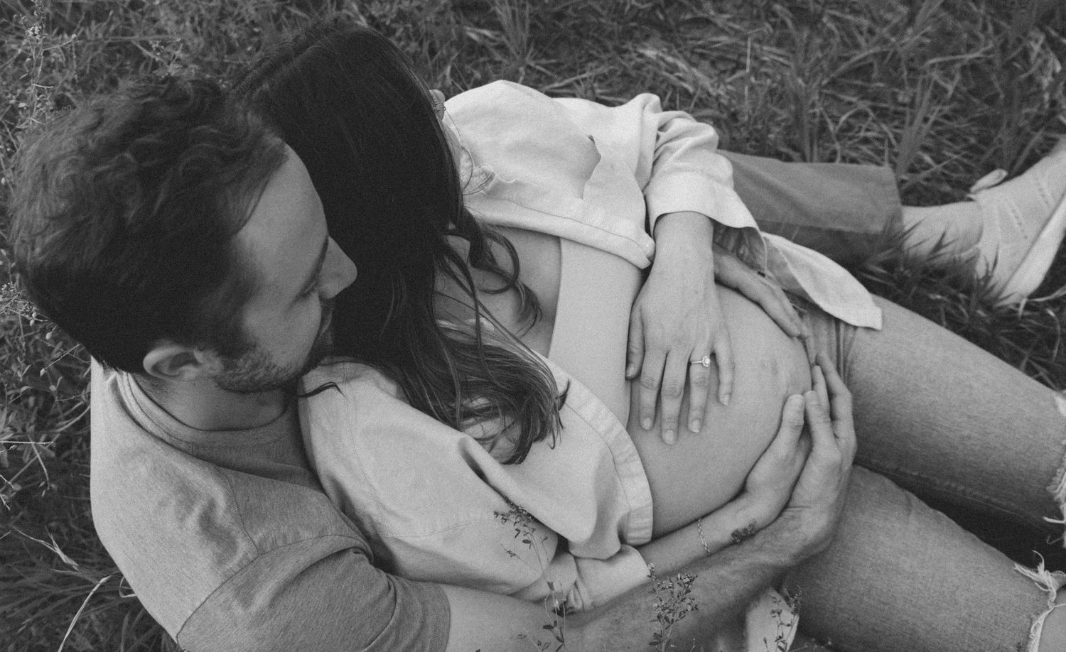 A couple lies together on grass in an intimate black and white photograph showing tender affection.