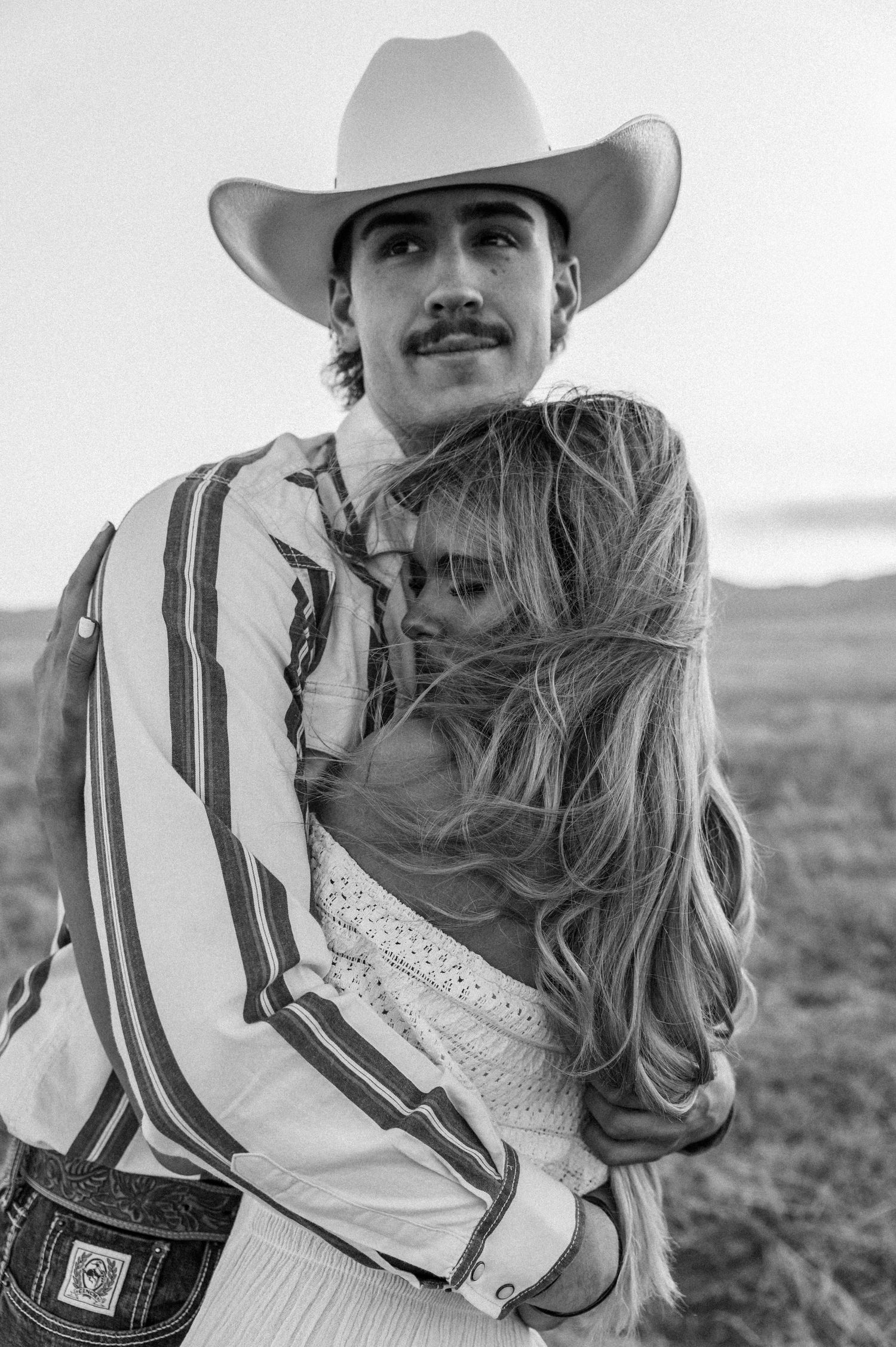 A black and white photo series shows a romantic western couple in cowboy hats embracing outdoors.