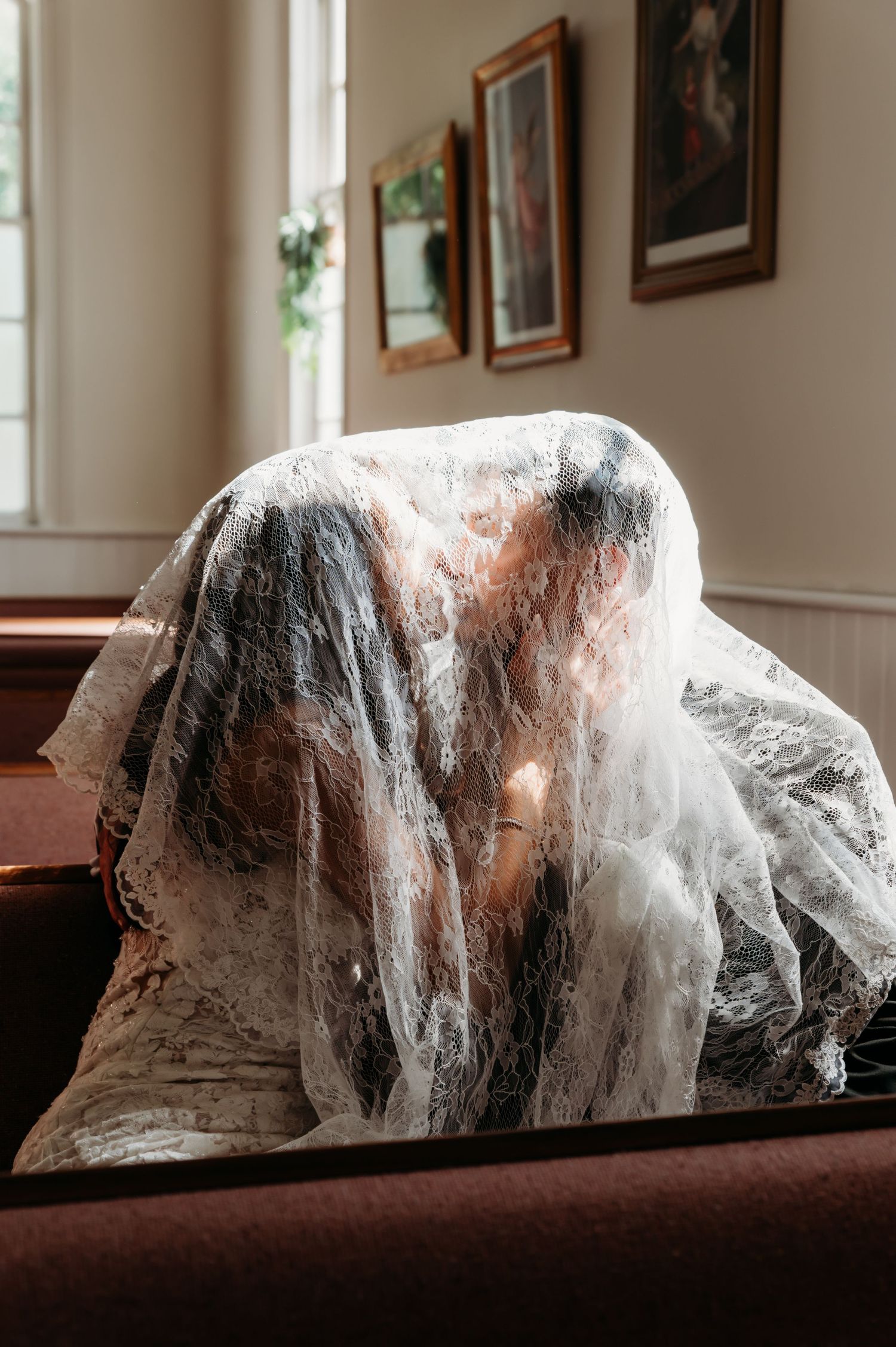 A bride and groom share a kiss under a lace veil in a church pew, creating an intimate wedding moment.