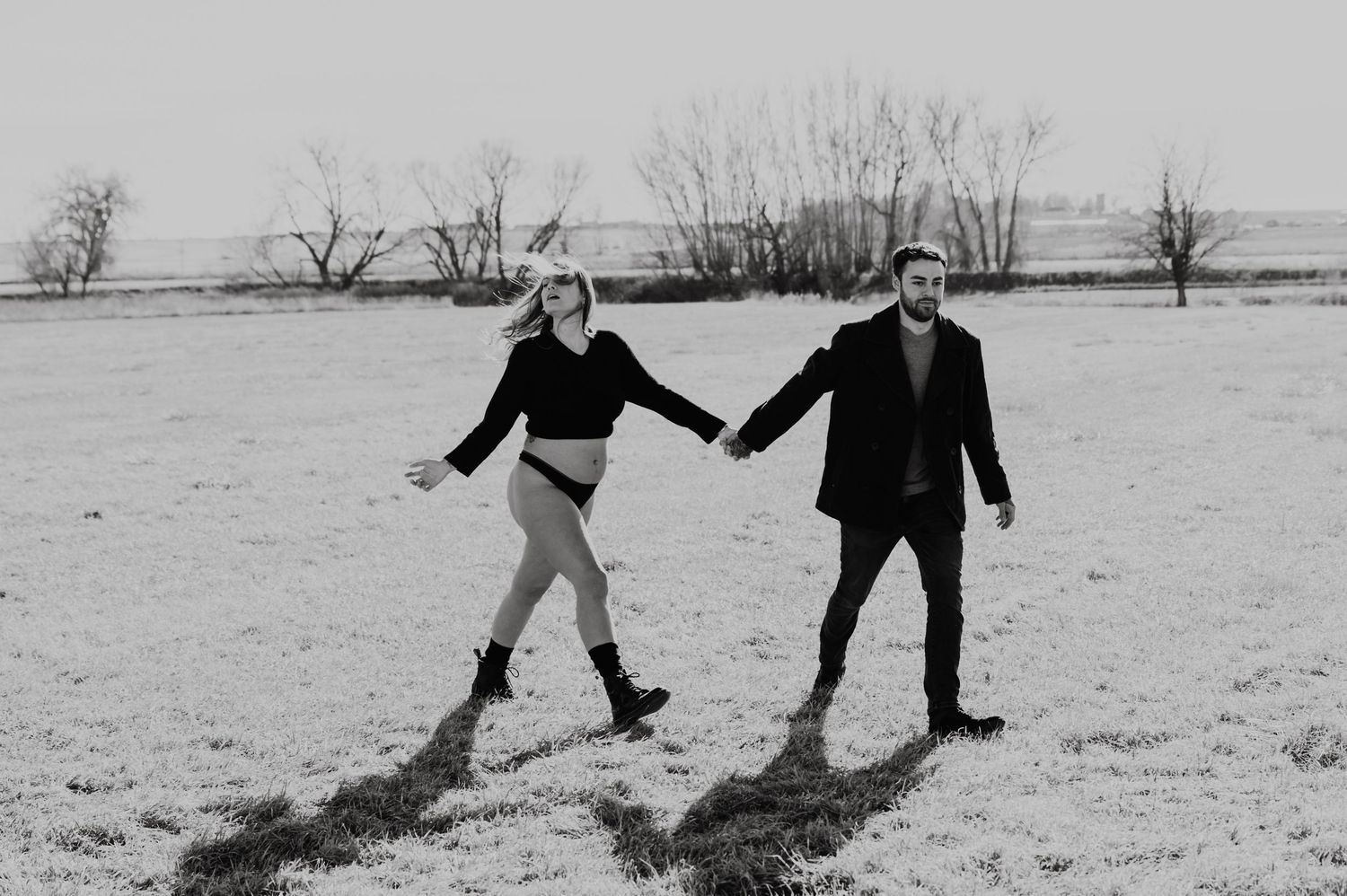 Two figures hold hands and playfully fall backwards together in the snow, shown in a black and white photo sequence.