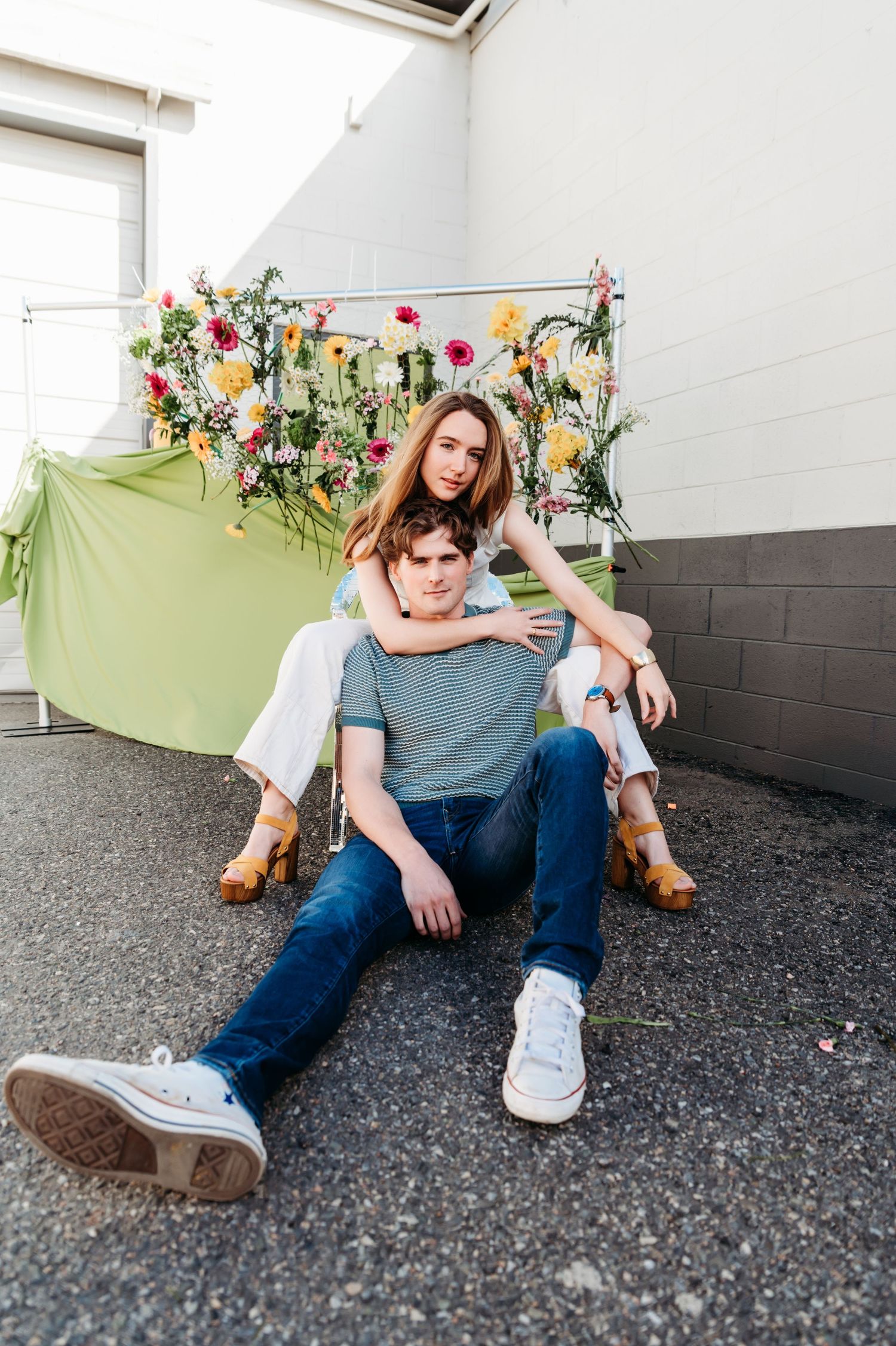 Couple poses casually against a wall decorated with colorful flowers.