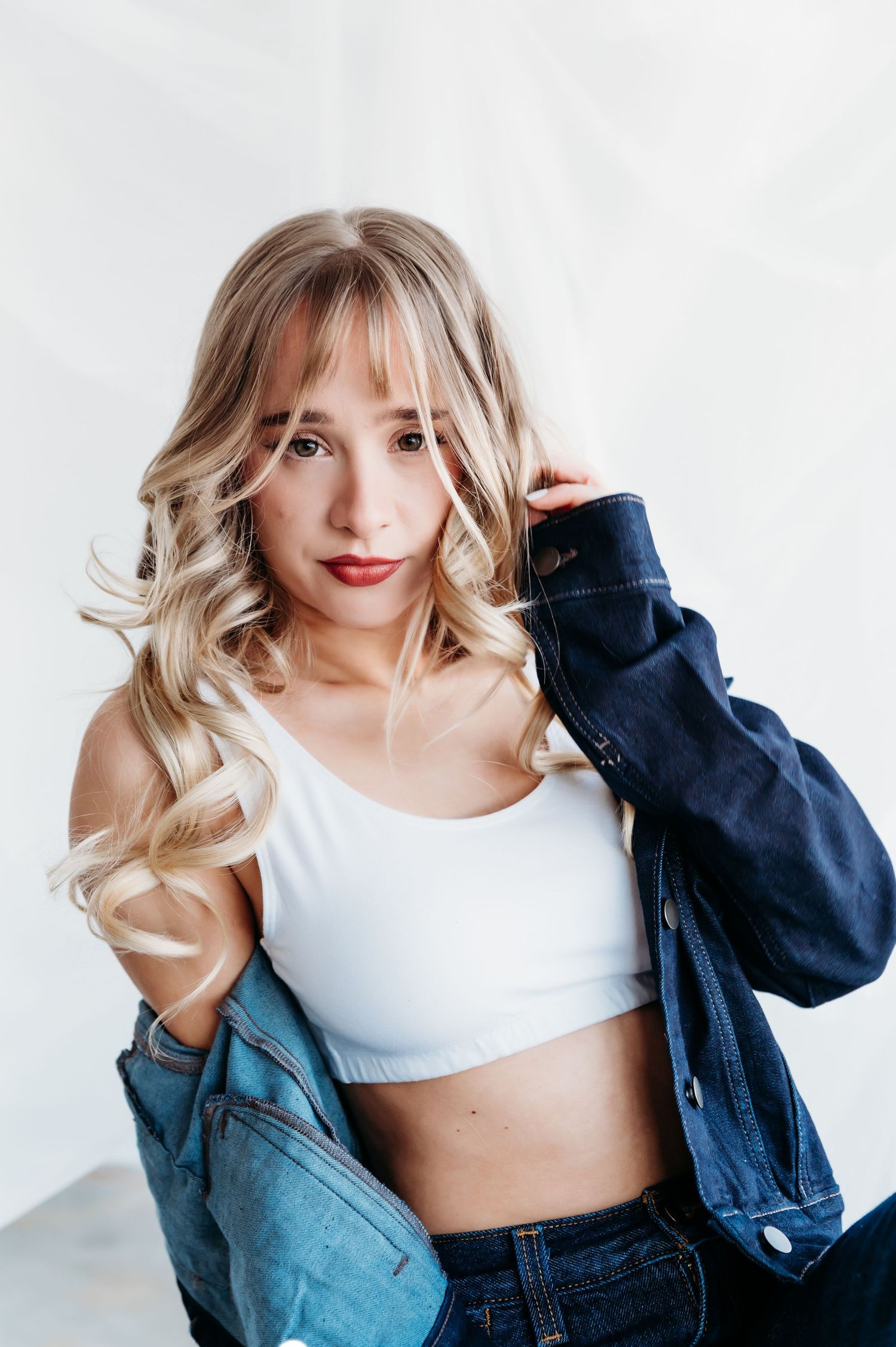 Fashion portrait of a person in crop top and denim jacket with styled blonde waves.