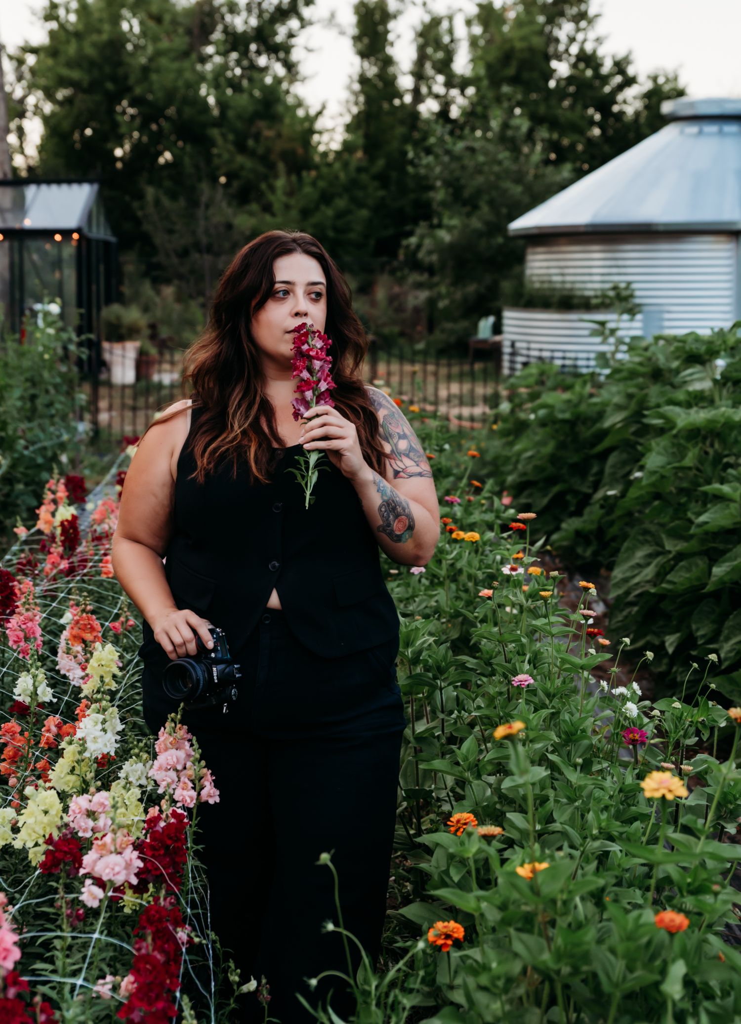 A woman in a black dress stands among a colorful wildflower garden filled with dahlias and marigolds.