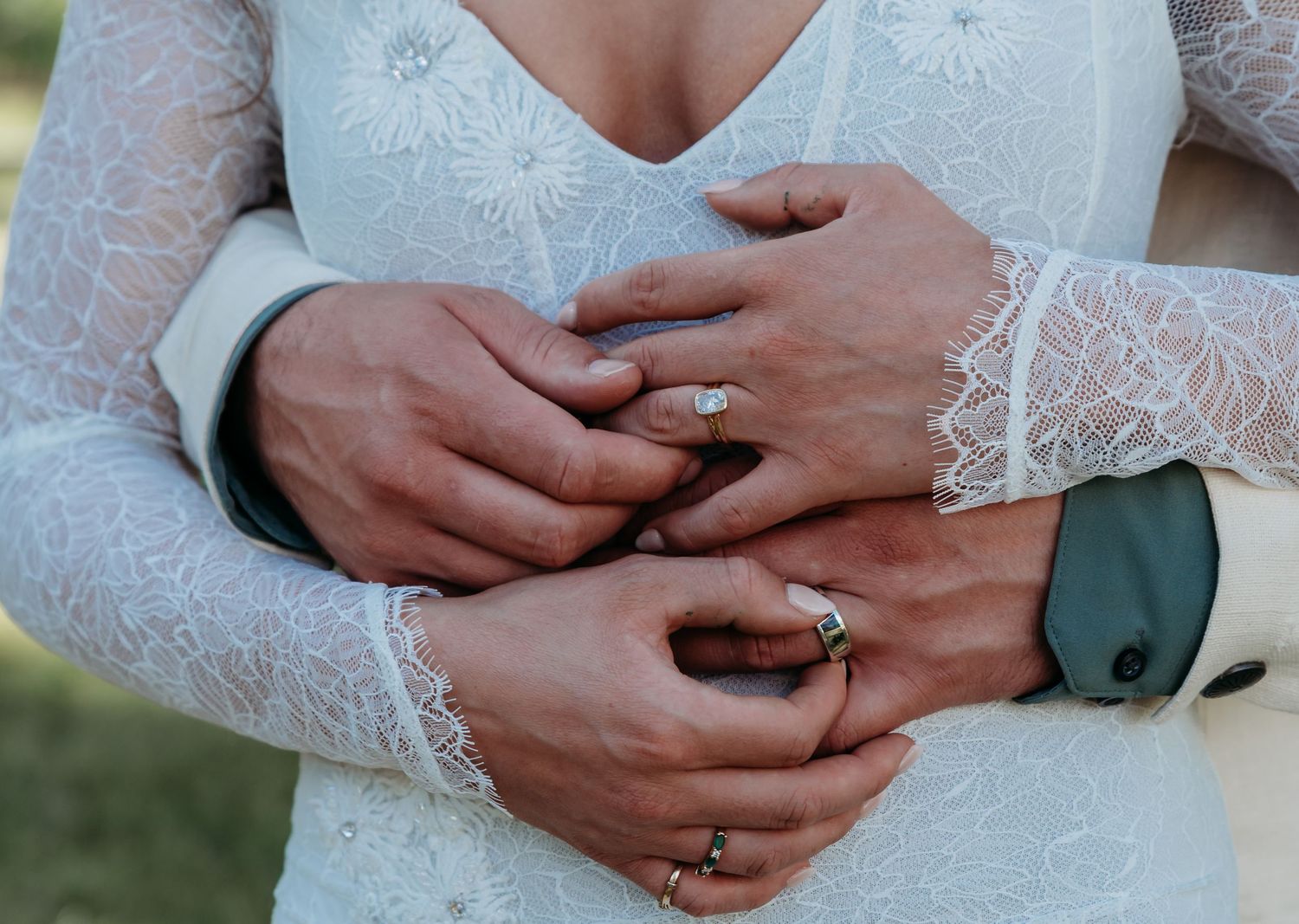 Close-up of newlyweds hands showing wedding rings, bride in lace gown, romantic wedding detail photo.