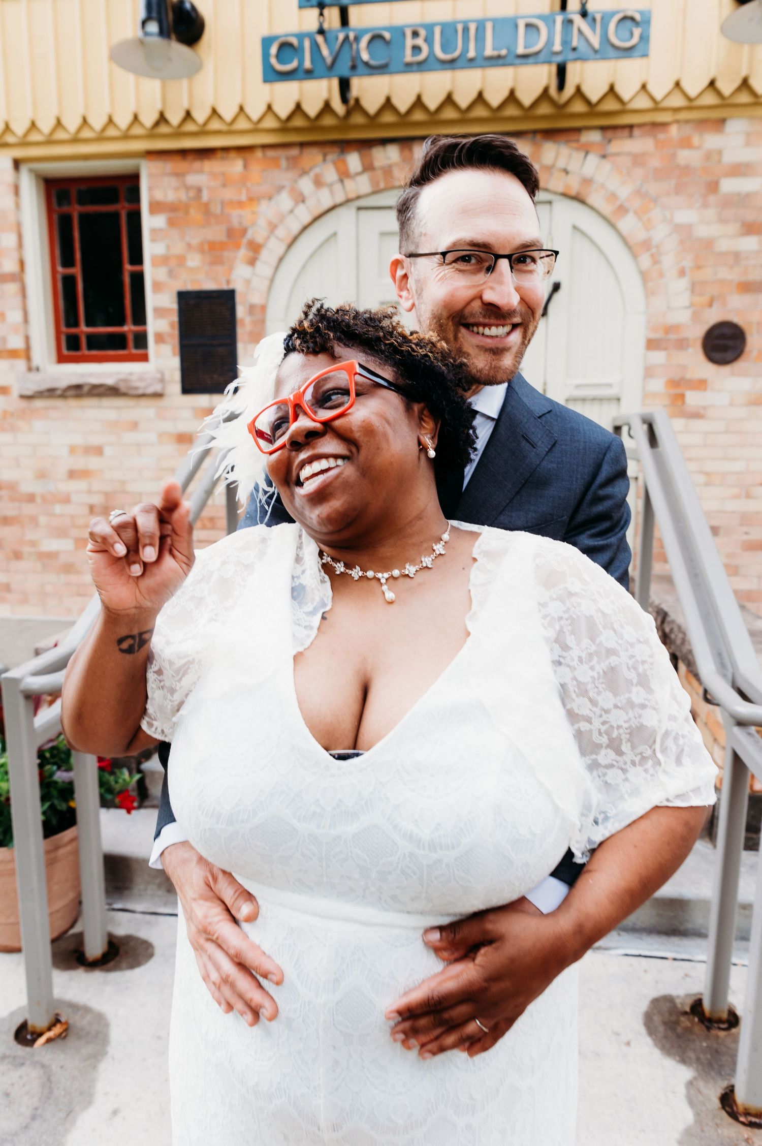 Two happy newlyweds share a candid laughing moment together at their wedding reception outside a brick building.