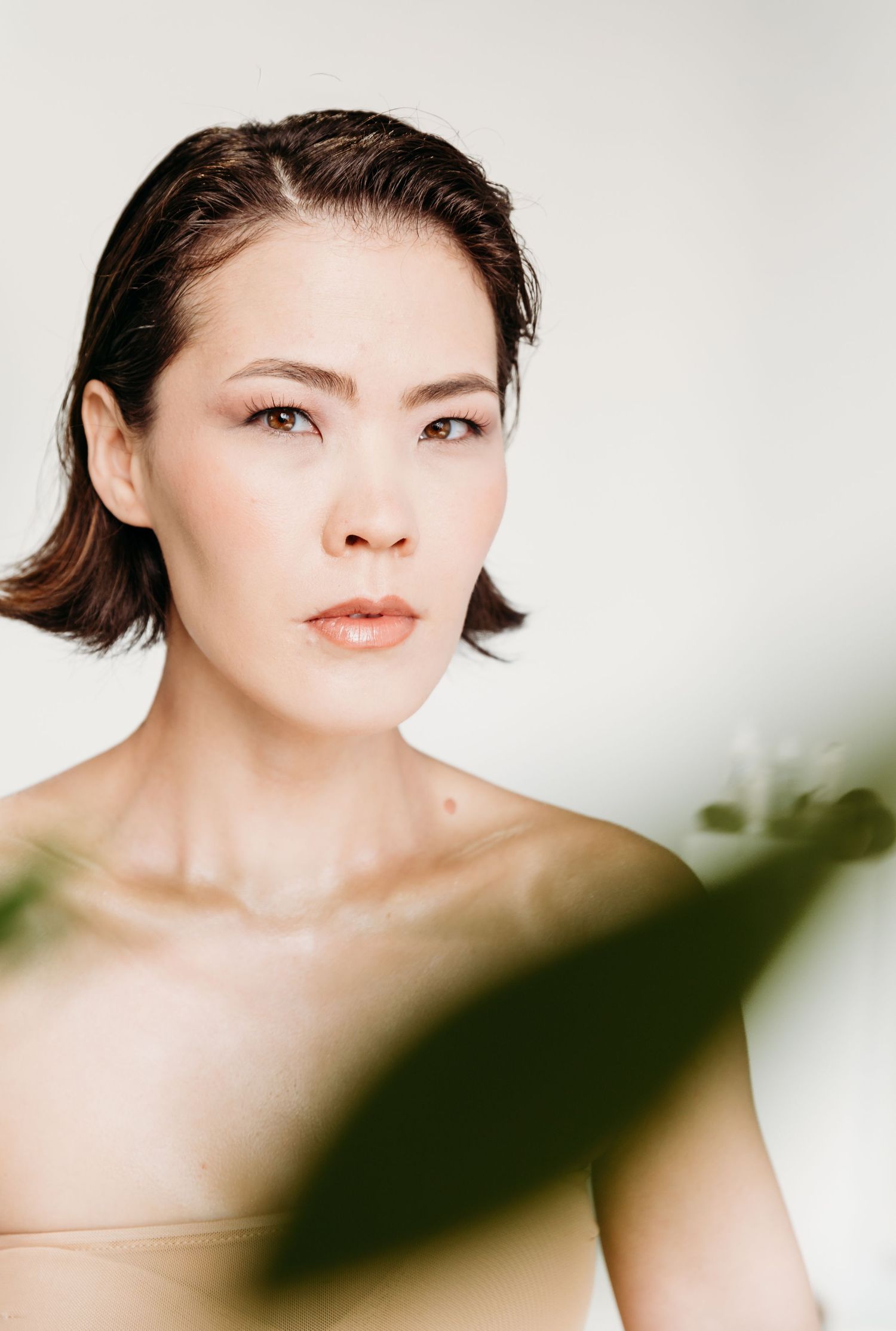 Close-up portrait of a young Asian woman with short dark hair, natural makeup, and bare shoulders against a white background.